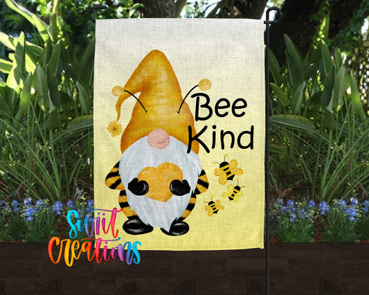 A garden flag featuring a gnome with a yellow hat and a bee on its back, surrounded by flowers and greenery.