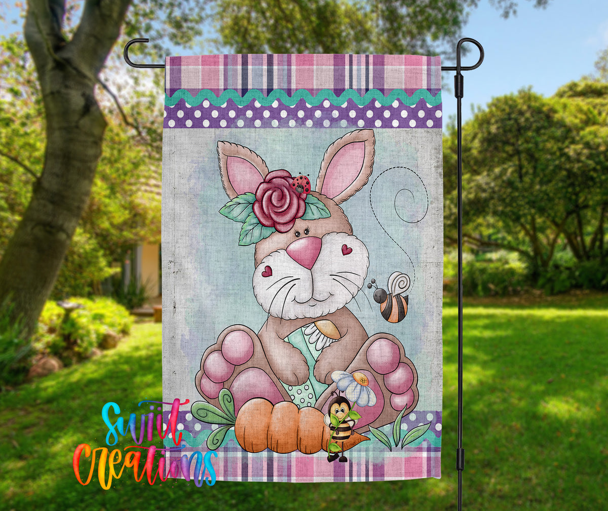 A colorful garden flag featuring a cartoon rabbit with a flower in its ear, surrounded by various garden elements such as a bee, a snail, and a pumpkin.