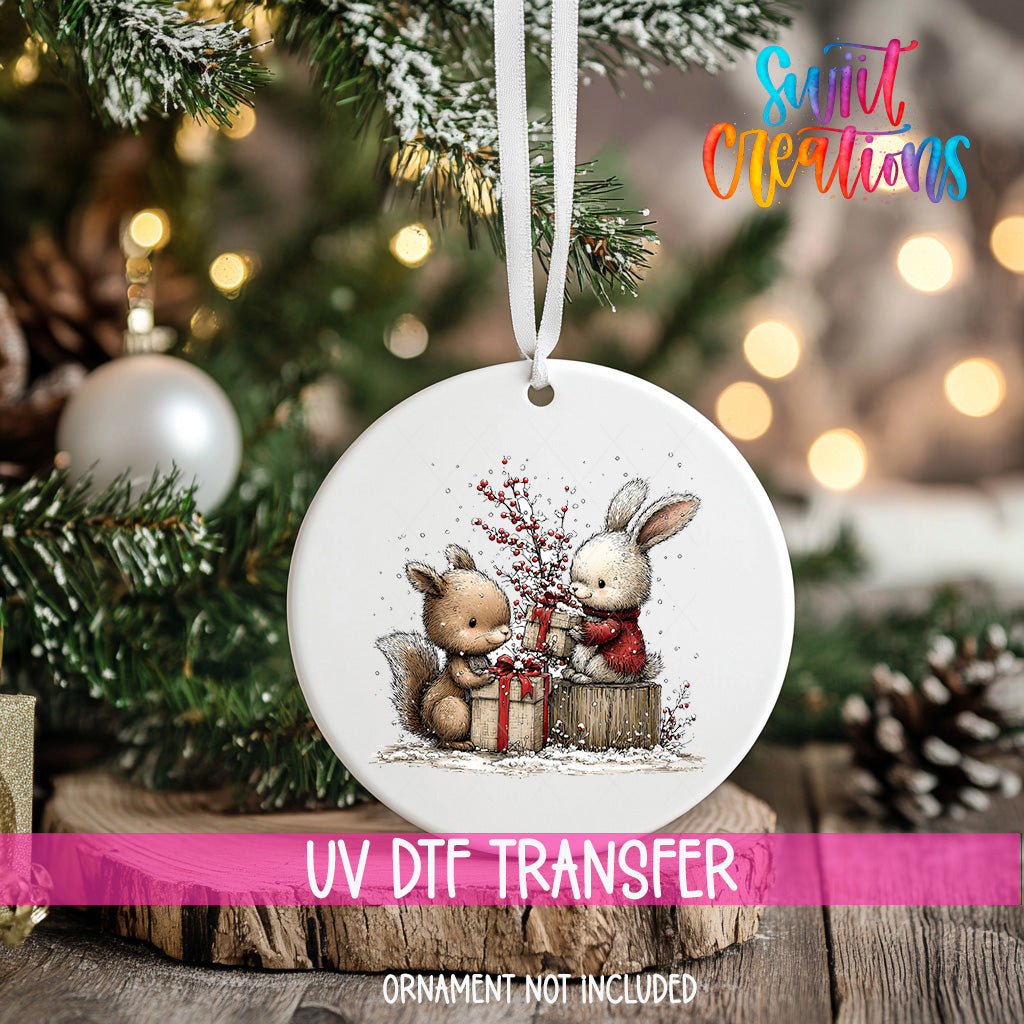A white ornament with a picture of two rabbits, one holding a gift, hanging on a Christmas tree.