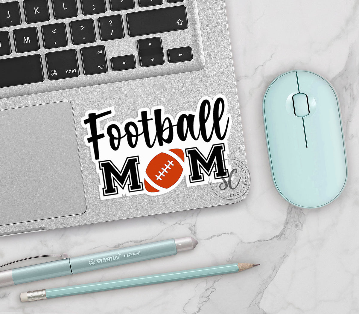 Football Mom vinyl sticker on a silver laptop next to a mint mouse and pens