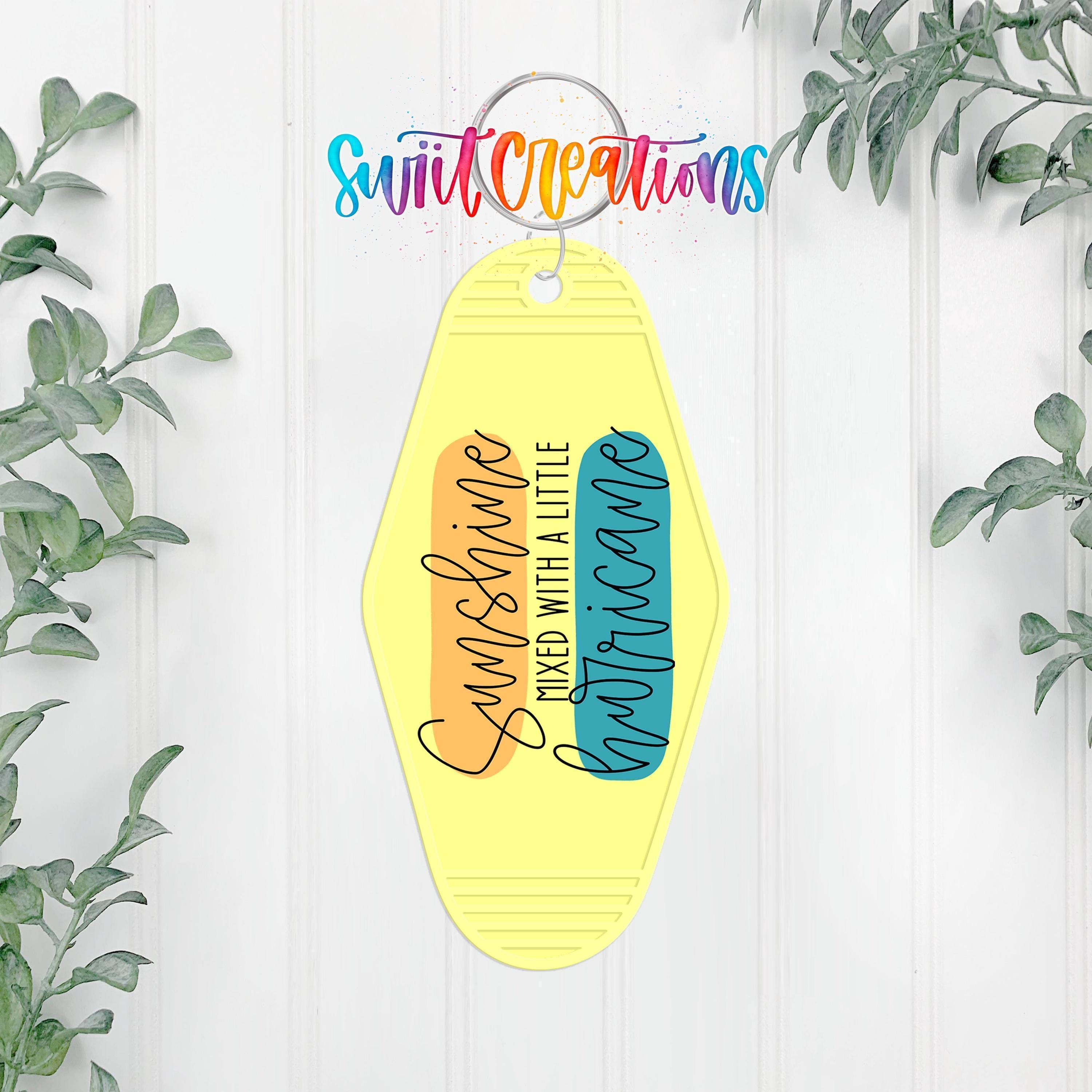 A keychain with a yellow and orange design hangs on a white wall, surrounded by green plants.