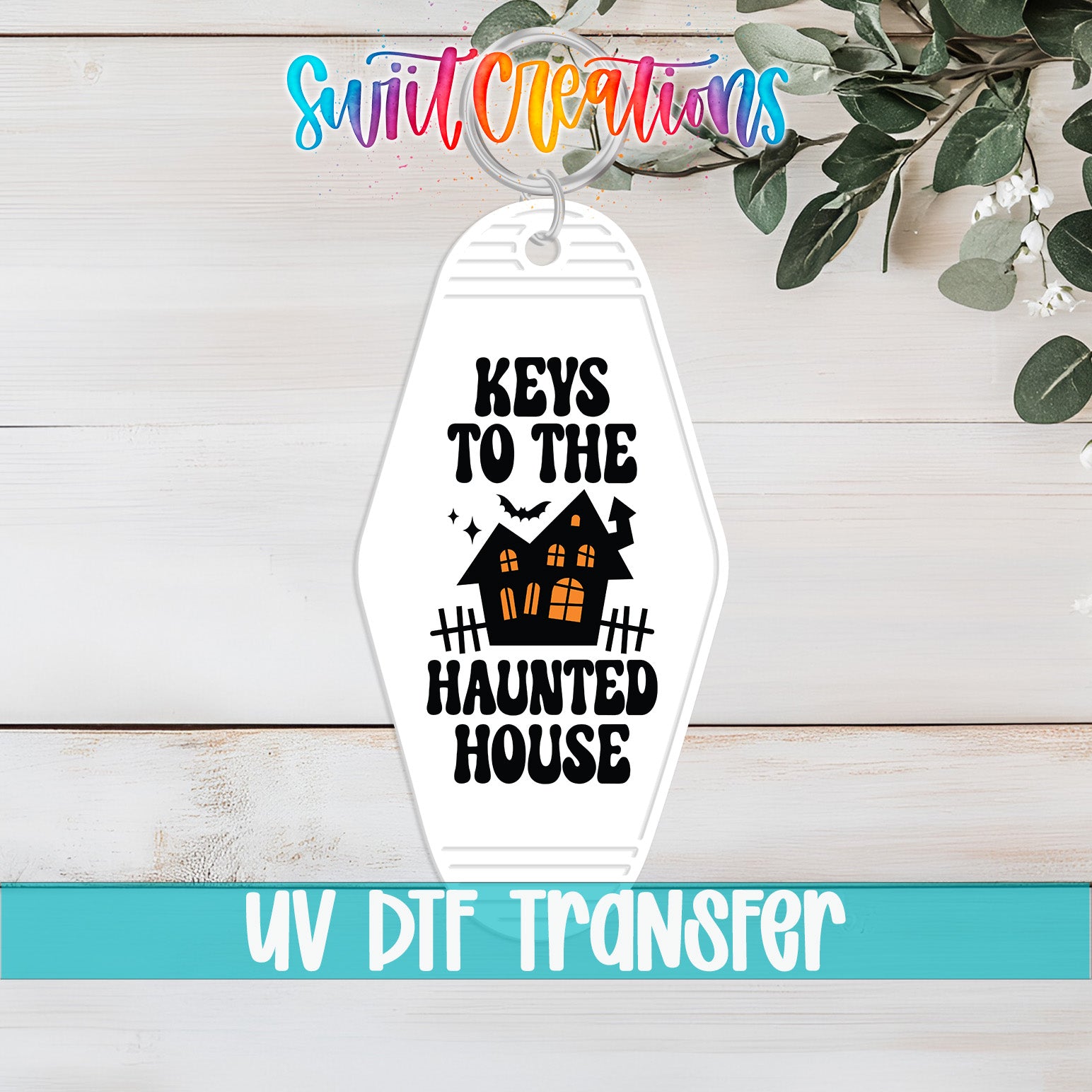 A keychain with the text "KEYS TO THE HAUNTED HOUSE" printed on it, along with a house illustration. The keychain is placed on a wooden surface, and there is a plant in the background.