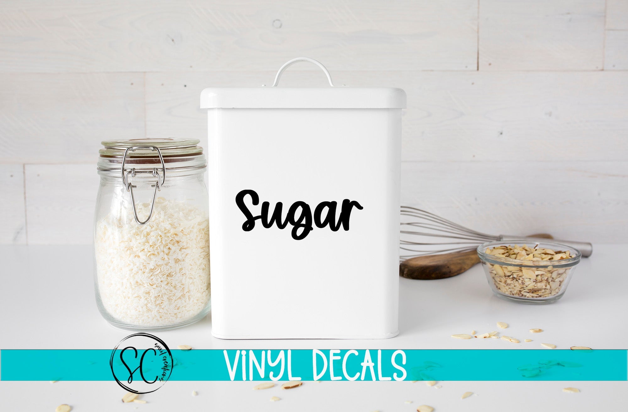 a white canister labeled "Sugar" next to a glass jar filled with white rice, a whisk, and a small glass bowl containing nuts. The background is a white wooden surface with scattered nuts.