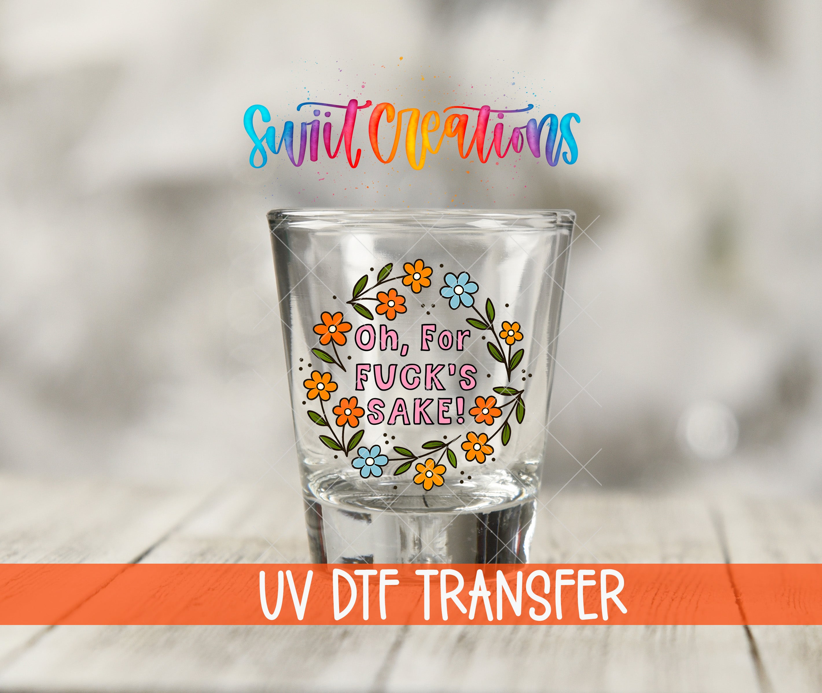 A shot glass with a colorful floral design and text on it, placed on a wooden surface.