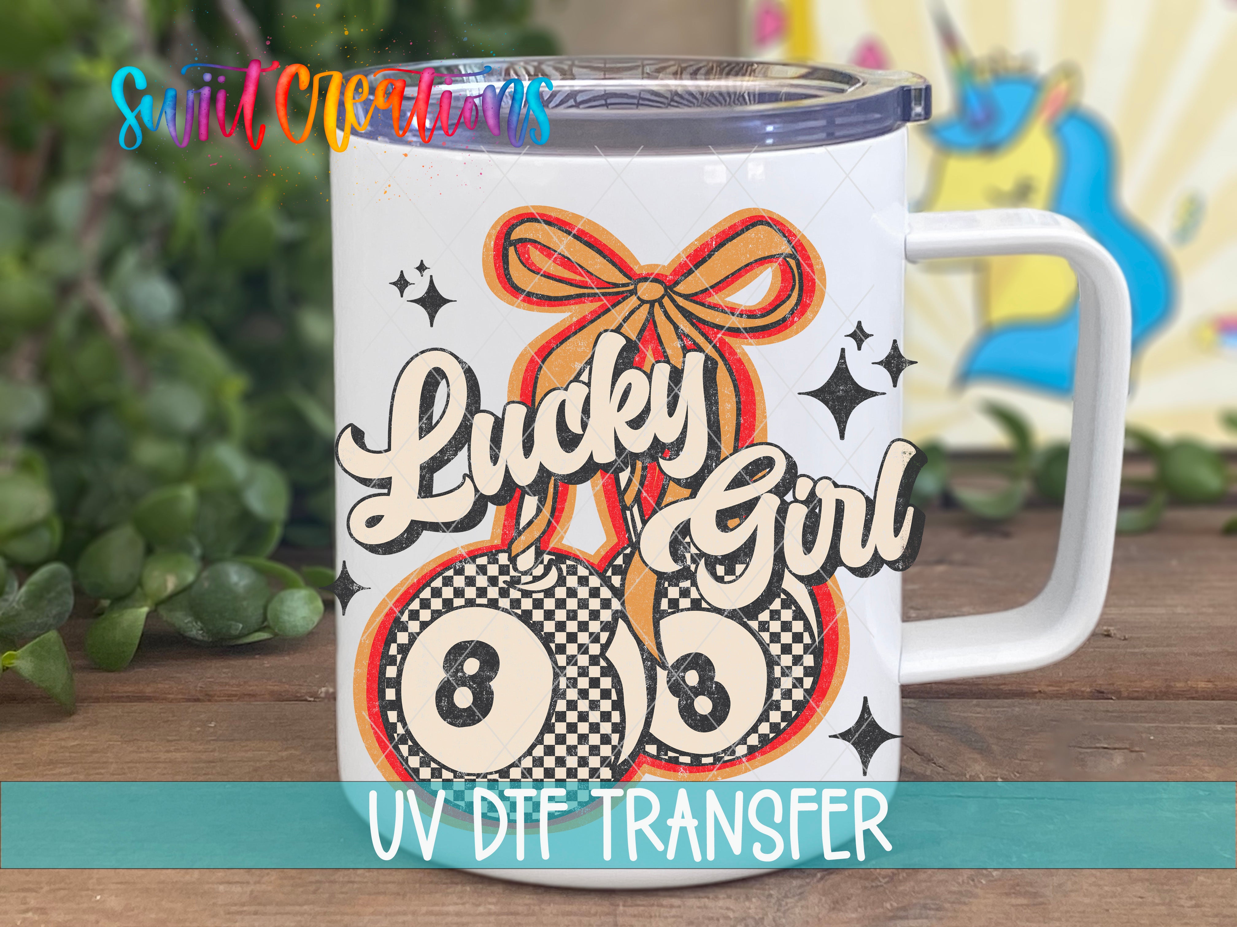 A white mug with a colorful design featuring a ribbon, stars, and the text "Lucky Girl" printed on it.