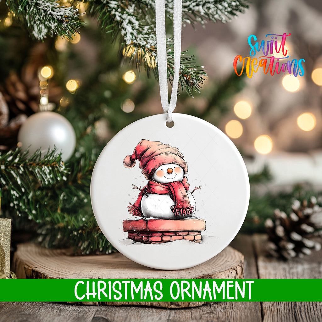 A white Christmas ornament featuring a snowman is hanging from a tree branch, with a blurred background of pine branches and twinkling lights.