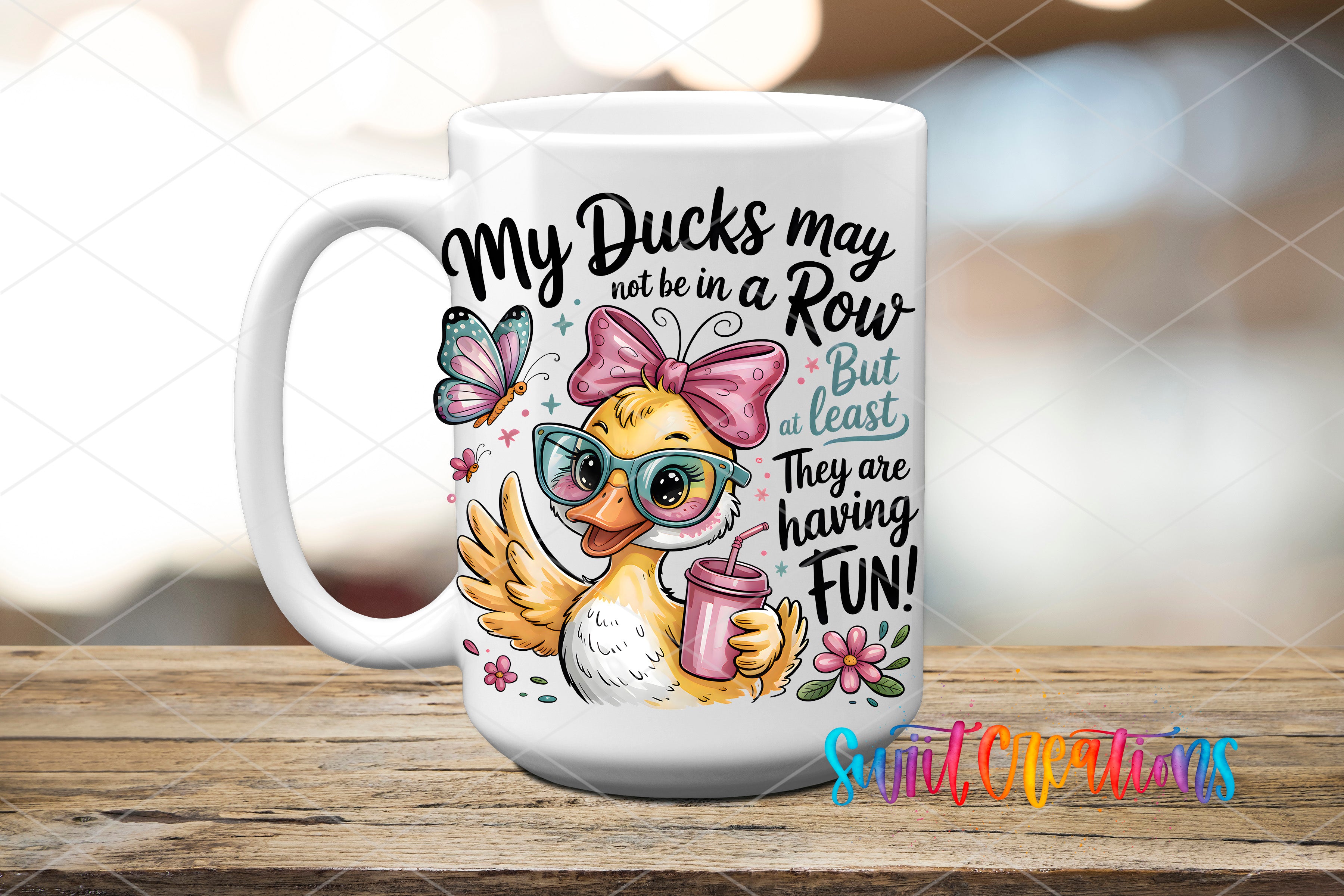 A white ceramic mug with a cartoon duck wearing sunglasses and holding a drink, surrounded by flowers and butterflies. The mug has text that reads "My Ducks may not be in a Row but at least they are having fun!"