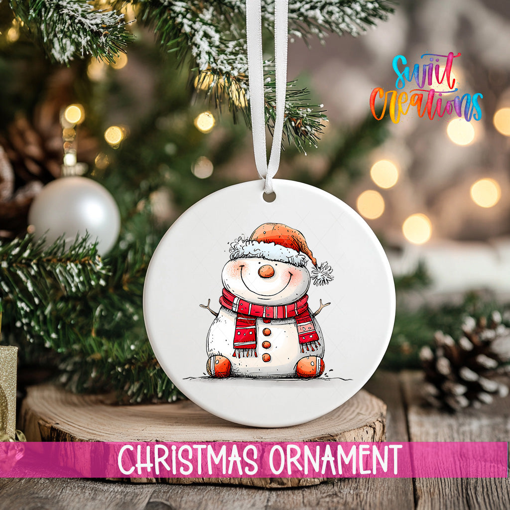 A white Christmas ornament featuring a smiling snowman is hanging from a ribbon, with a blurred background of a decorated Christmas tree and other ornaments.