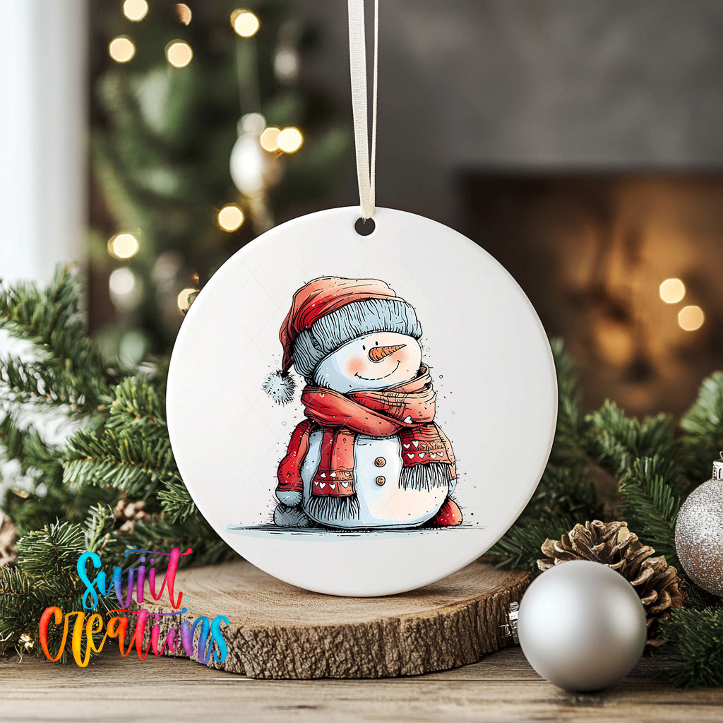 A white ceramic ornament featuring a snowman with a red scarf and hat, sitting on a wooden surface. The ornament is hanging from a string, and there are Christmas decorations and ornaments in the background.