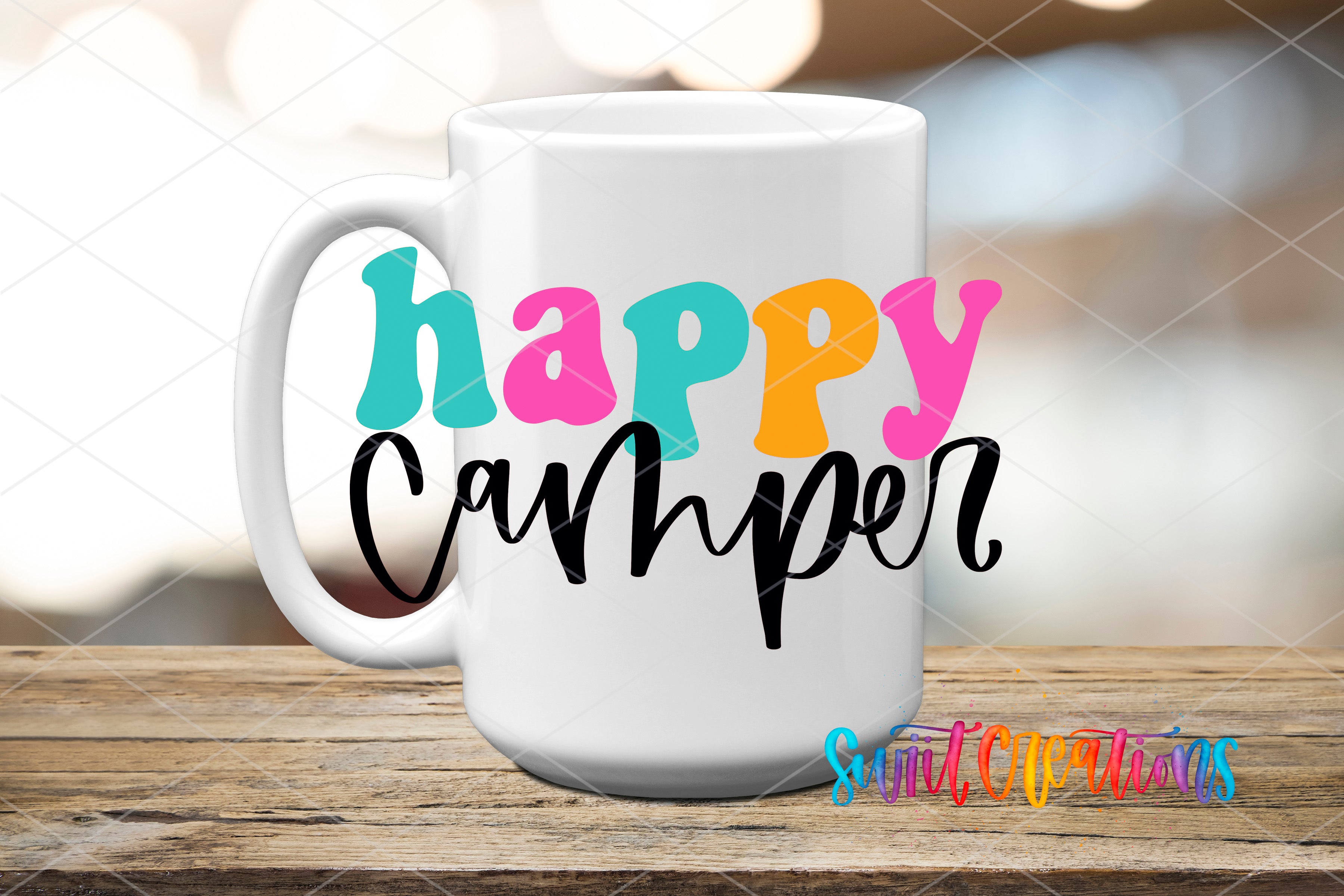 A white mug with colorful text that says "happy camper" on it, placed on a wooden surface.