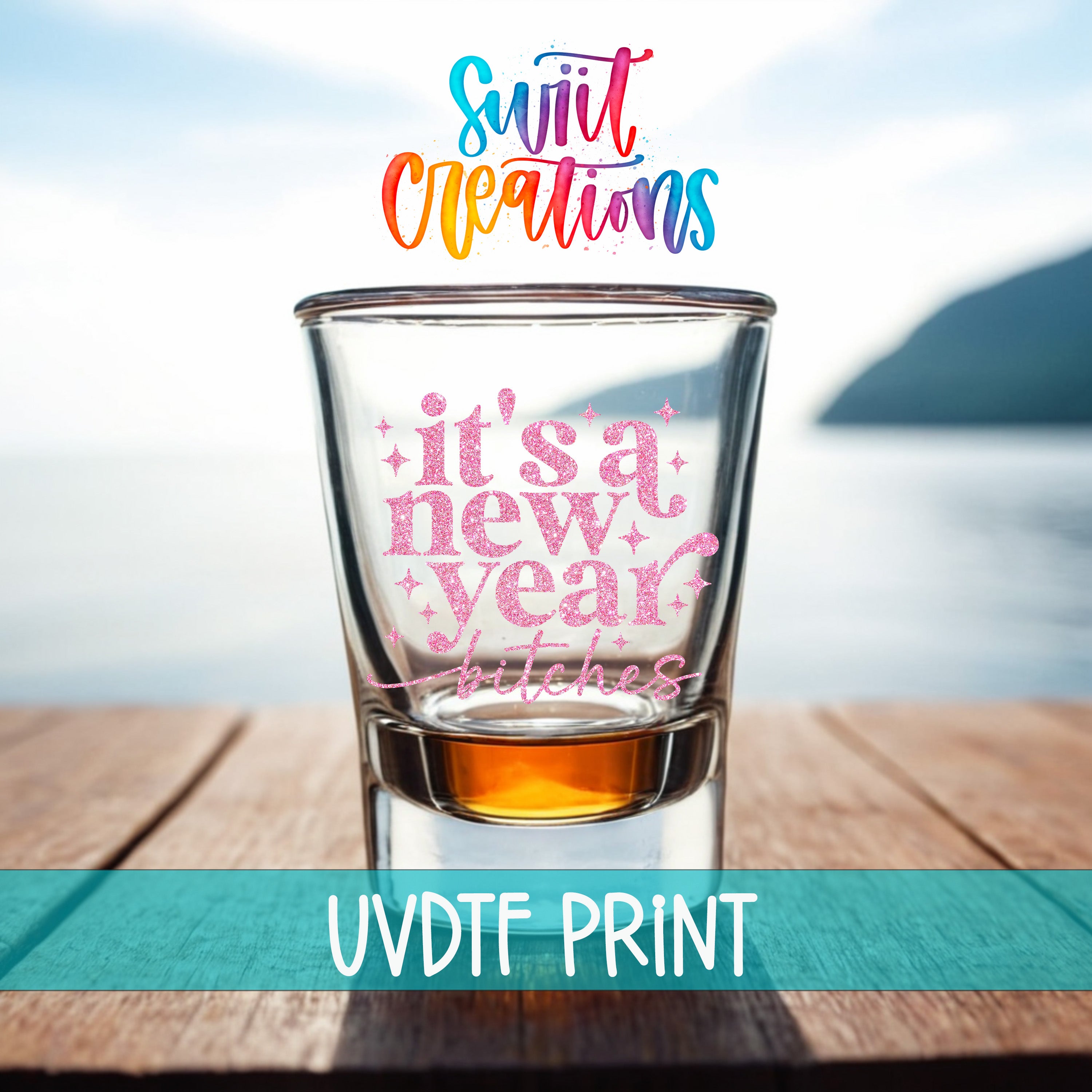 A shot glass with a colorful design on it, placed on a wooden surface with a body of water in the background.