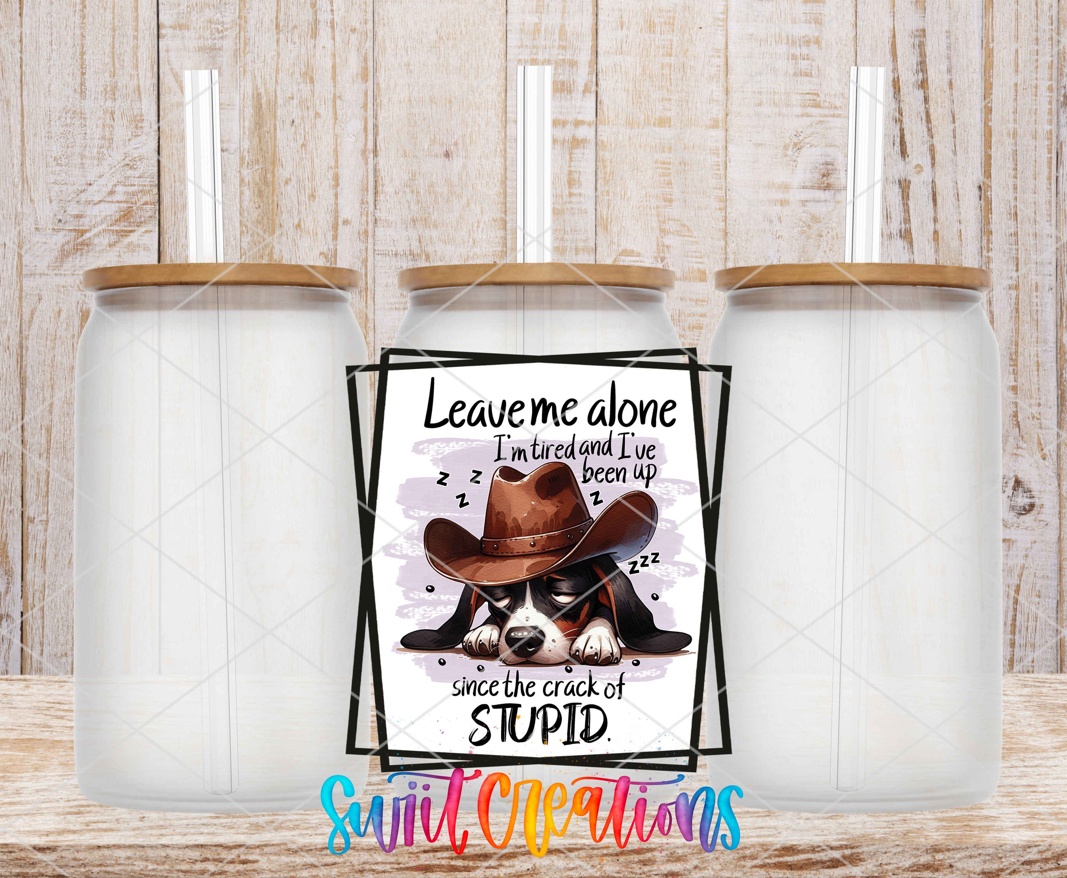 a sign with a cartoon image of a dog wearing a cowboy hat and the text "Leave me alone I'm tired and I've been up since the crack of stupid". The sign is placed between two empty glass jars with wooden lids.