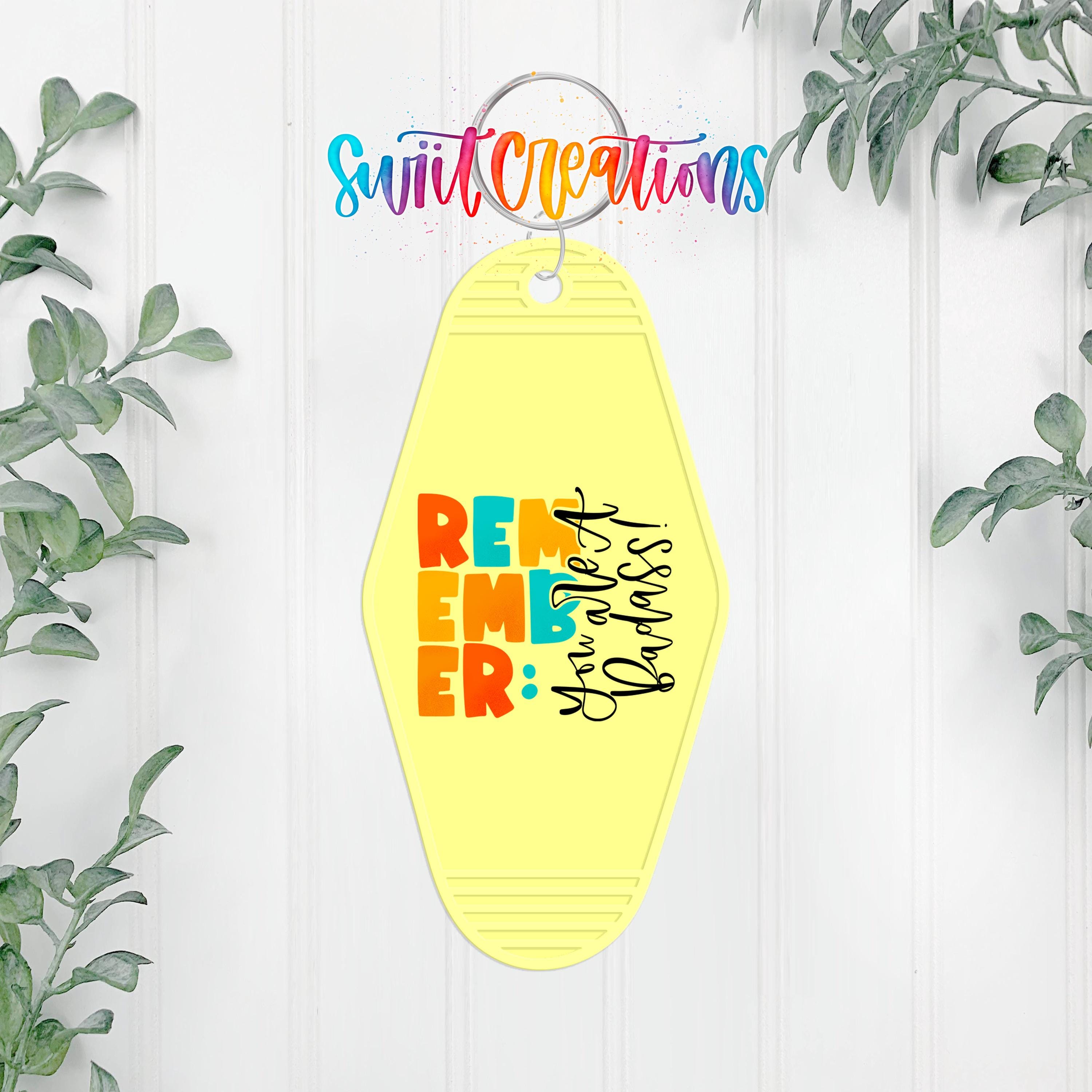 A yellow keychain with the text "REMEMBER" in large letters, surrounded by colorful text and a decorative border.