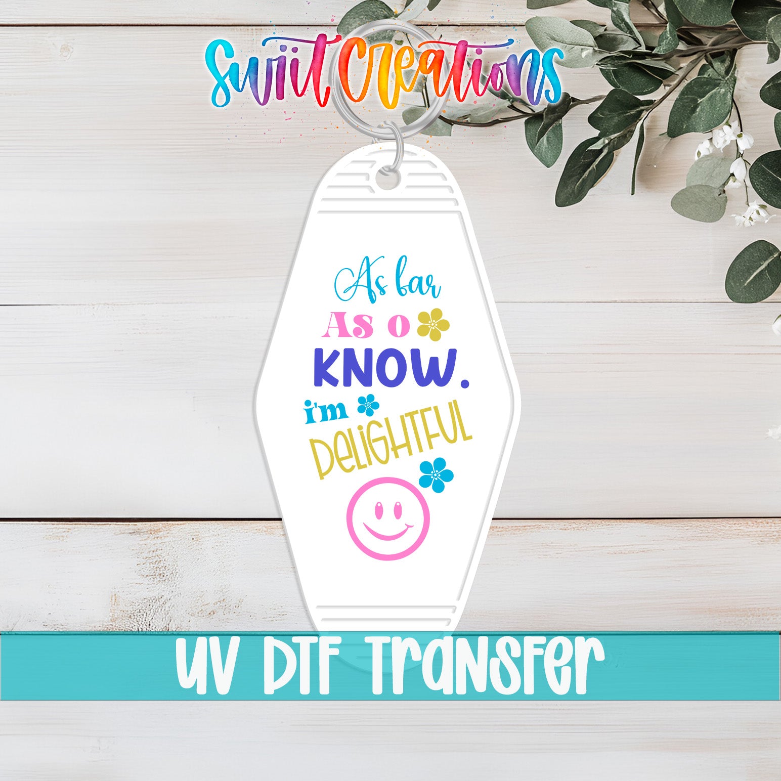 A keychain with a colorful design and text, placed on a wooden surface with greenery in the background.