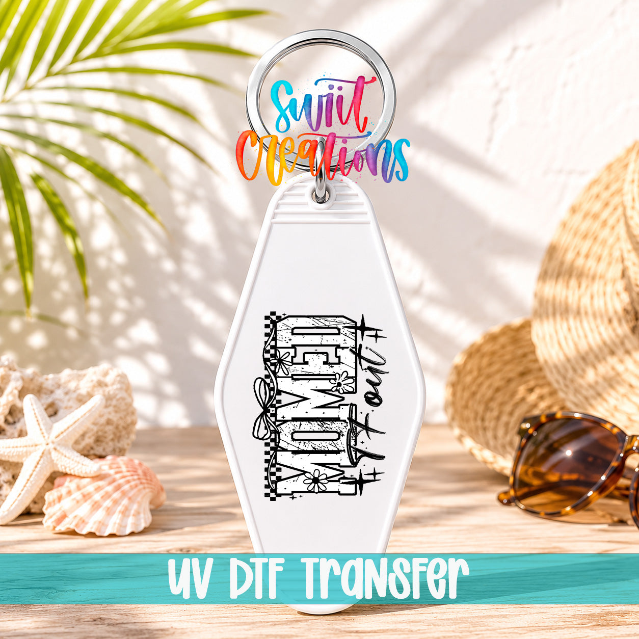 A white keychain with a colorful design and text, placed on a wooden surface with sunglasses, a straw hat, and seashells in the background.