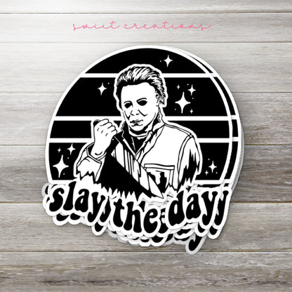 Stack of Slay the Day glossy stickers on a gray wood table