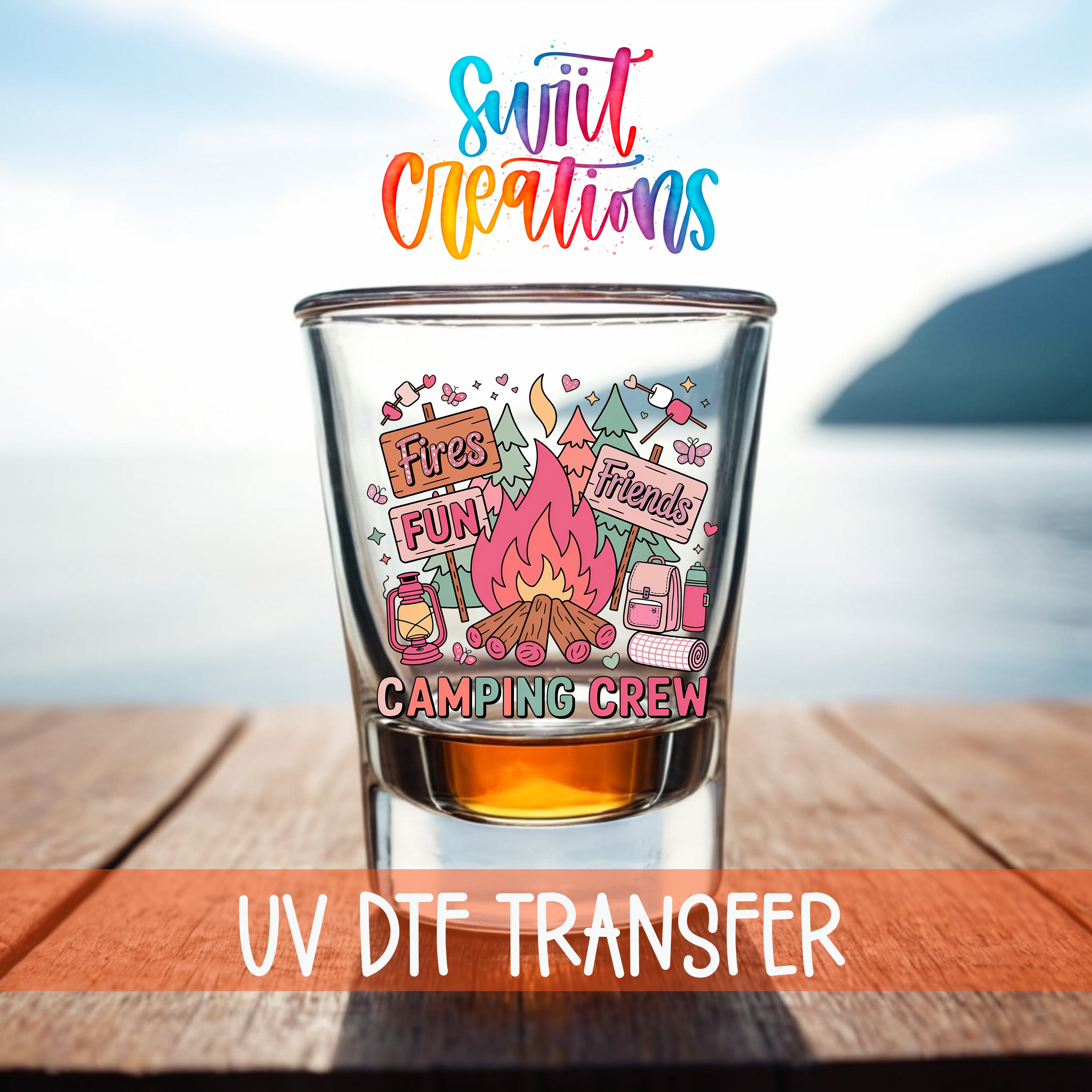 A glass tumbler with a colorful design featuring camping-related items and text, placed on a wooden surface with a body of water in the background.