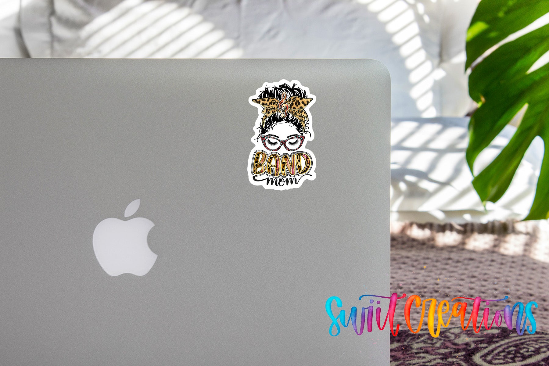 a sticker with a stylized face and the text "BAND MOM" on the back of a silver laptop.