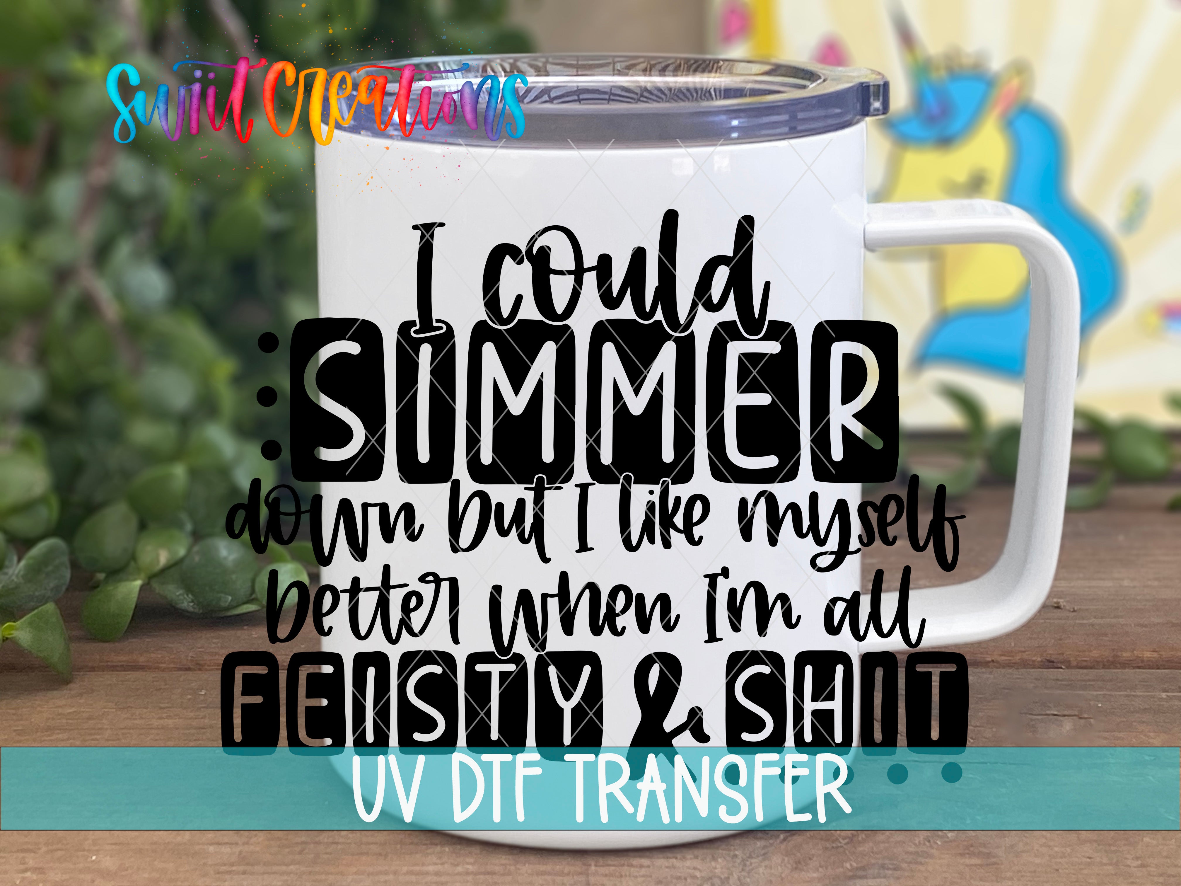 A white mug with a printed text design on it, placed on a wooden surface with greenery in the background.