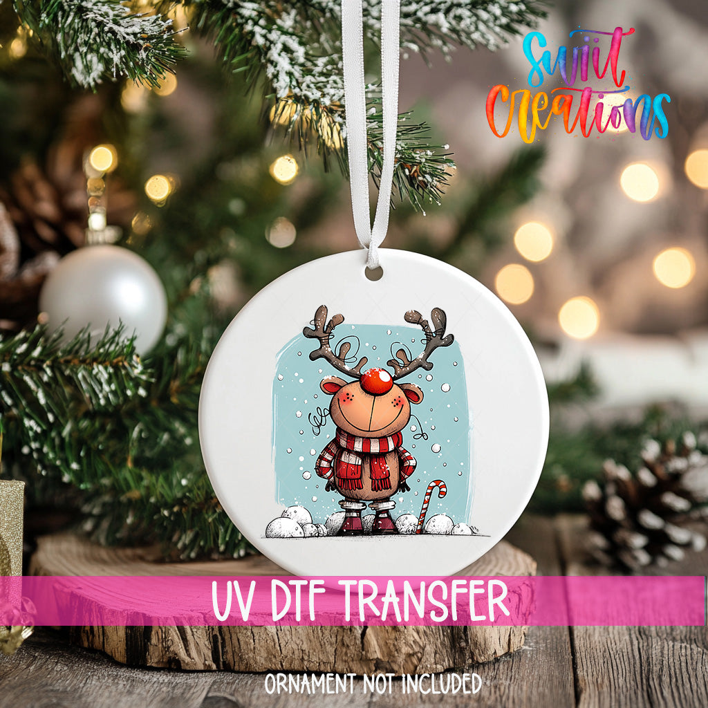 A white ornament with a cartoon reindeer and snowflakes hanging on a Christmas tree.