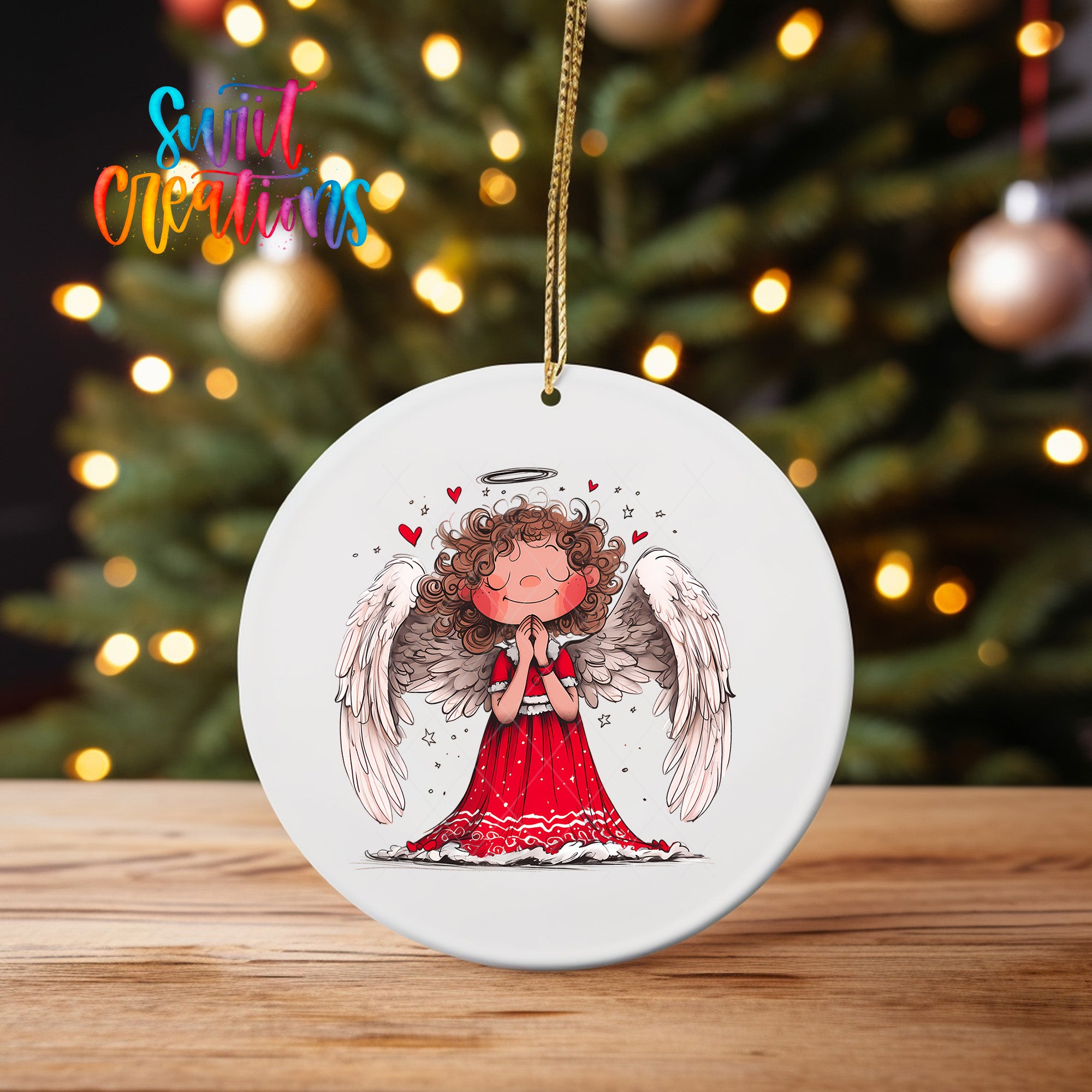 A white ceramic ornament featuring an illustration of a smiling, winged angel with curly hair and a halo, set against a blurred background of Christmas lights.