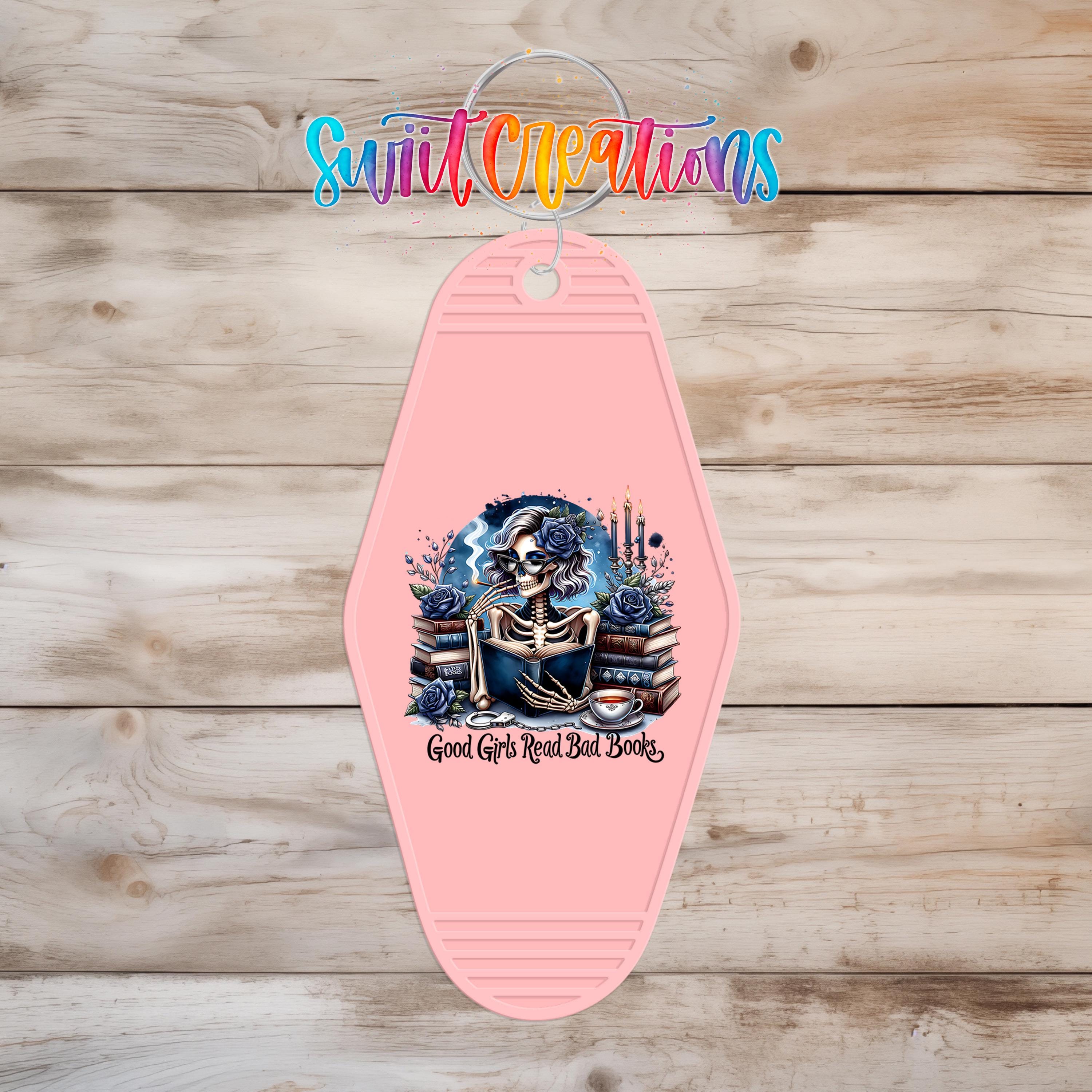 A pink keychain with a graphic design featuring a skeleton reading a book, surrounded by flowers and plants.