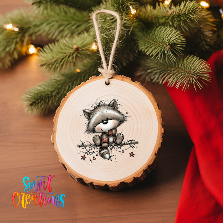 A wooden ornament with a raccoon sitting on a branch, surrounded by Christmas lights, is hanging on a Christmas tree.