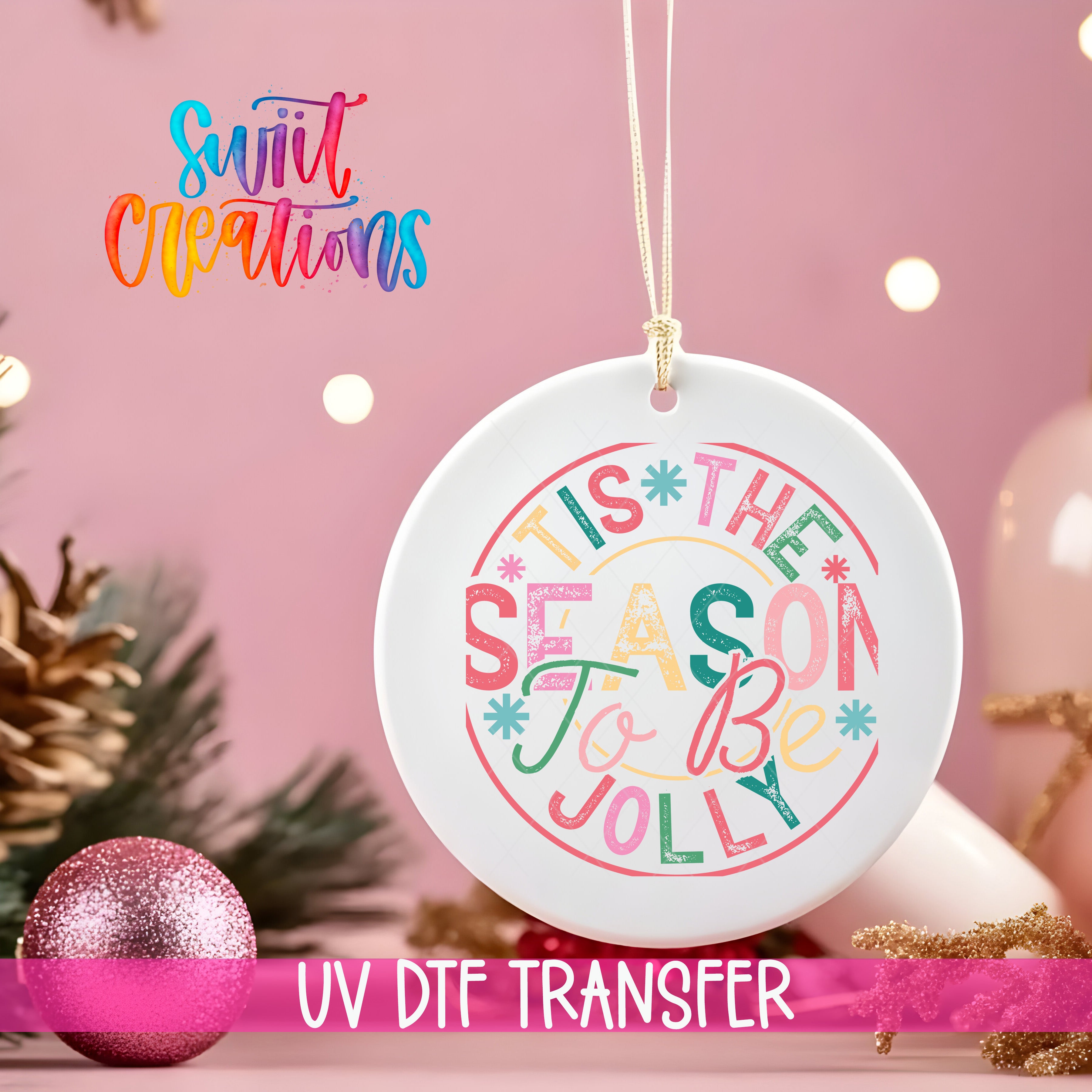 A white ceramic ornament with colorful text that says "THIS SEASON TO BE JOYFUL" hanging on a string. The ornament is surrounded by Christmas decorations, including a pink glitter ornament and pine cones.