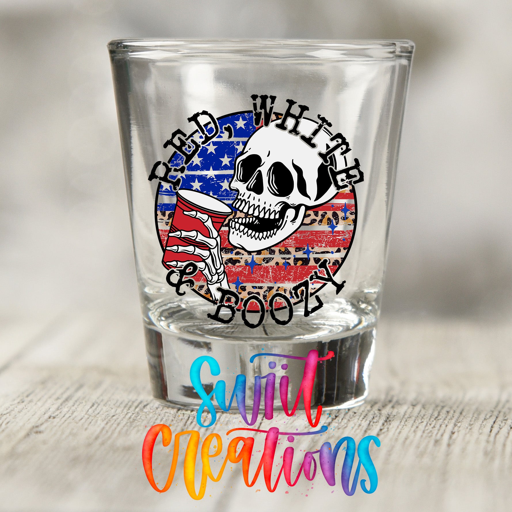 A shot glass with a skull design and the text "RED WHITE BOOZY" printed on it, along with a colorful text overlay that says "SWELL CREATIONS".