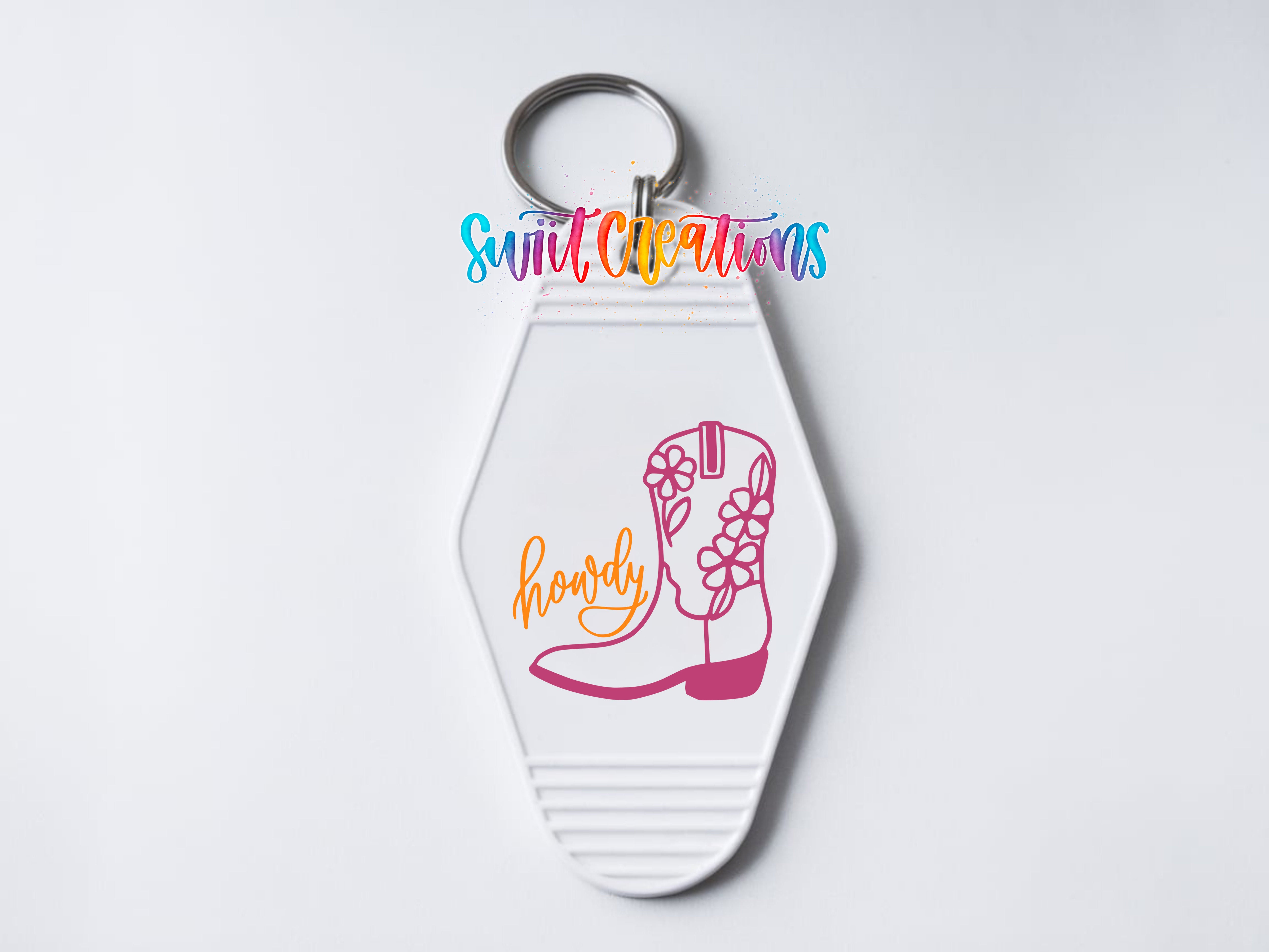 A keychain with a white hexagonal shape and a pink cowboy boot graphic on it. The word "howdy" is written below the boot.