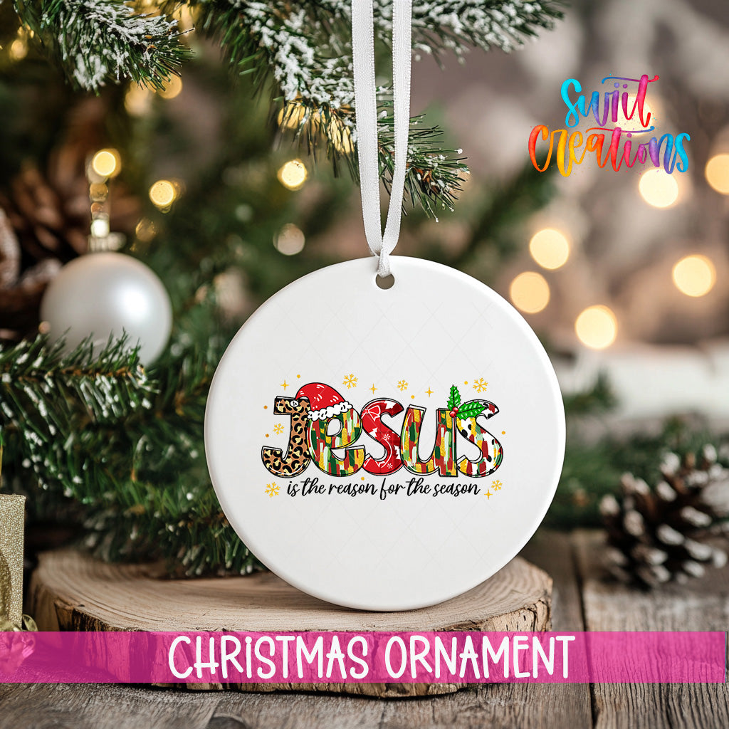 A white Christmas ornament with the word "JESUS" written on it, hanging from a tree branch.