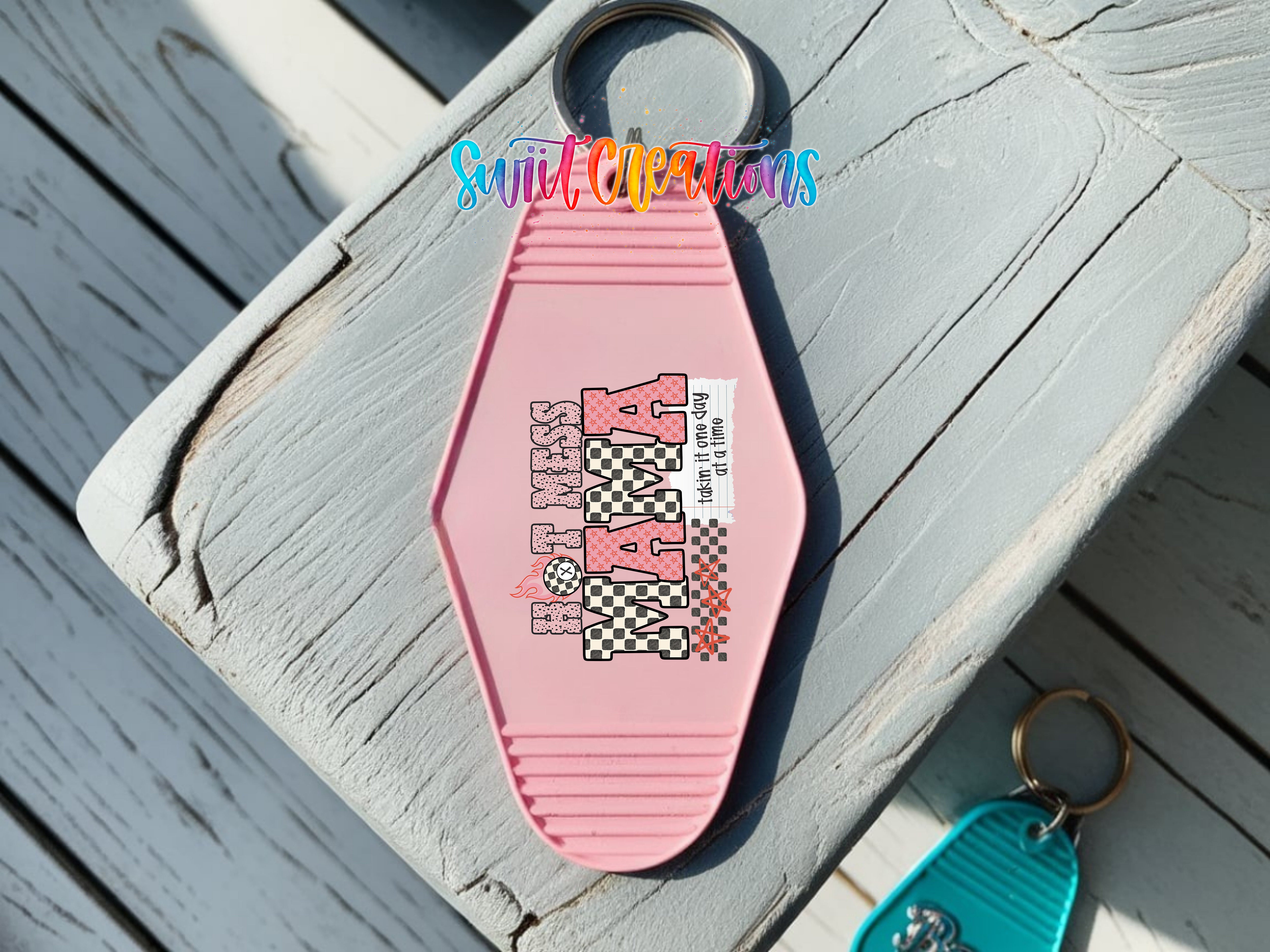 A pink keychain with a checkered pattern and the text "Hot Mess Mama" printed on it, placed on a wooden surface.