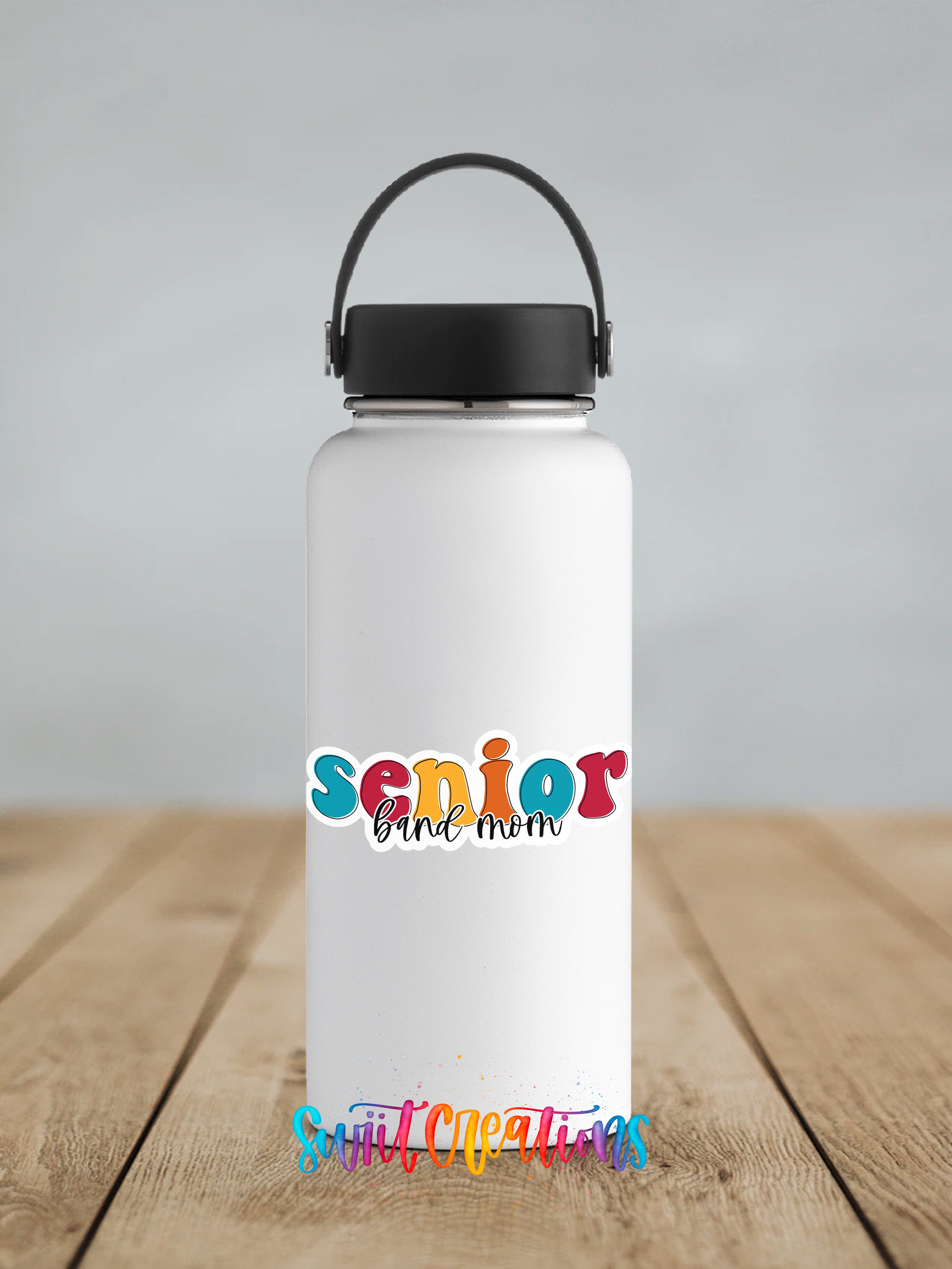 A white water bottle with a black handle and a colorful text logo that says " Senior band mom" on it, placed on a wooden surface.