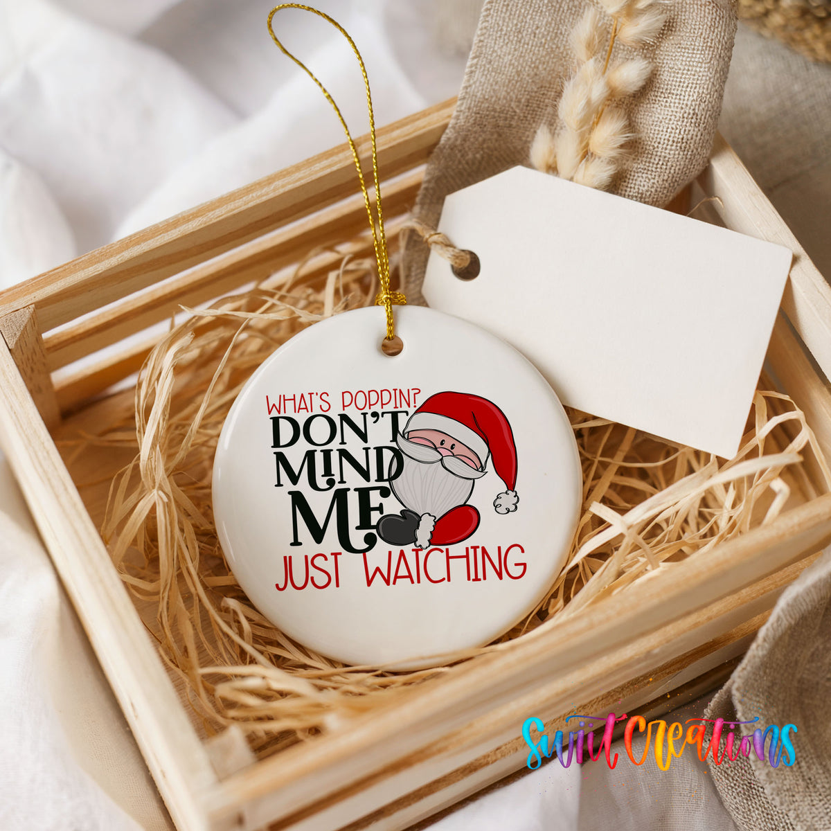 A white ceramic ornament with a humorous text design, placed in a wooden crate surrounded by straw.