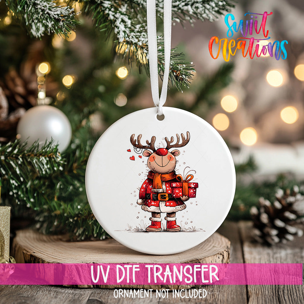 A white ceramic ornament with a cartoon reindeer holding a gift, hanging on a Christmas tree.