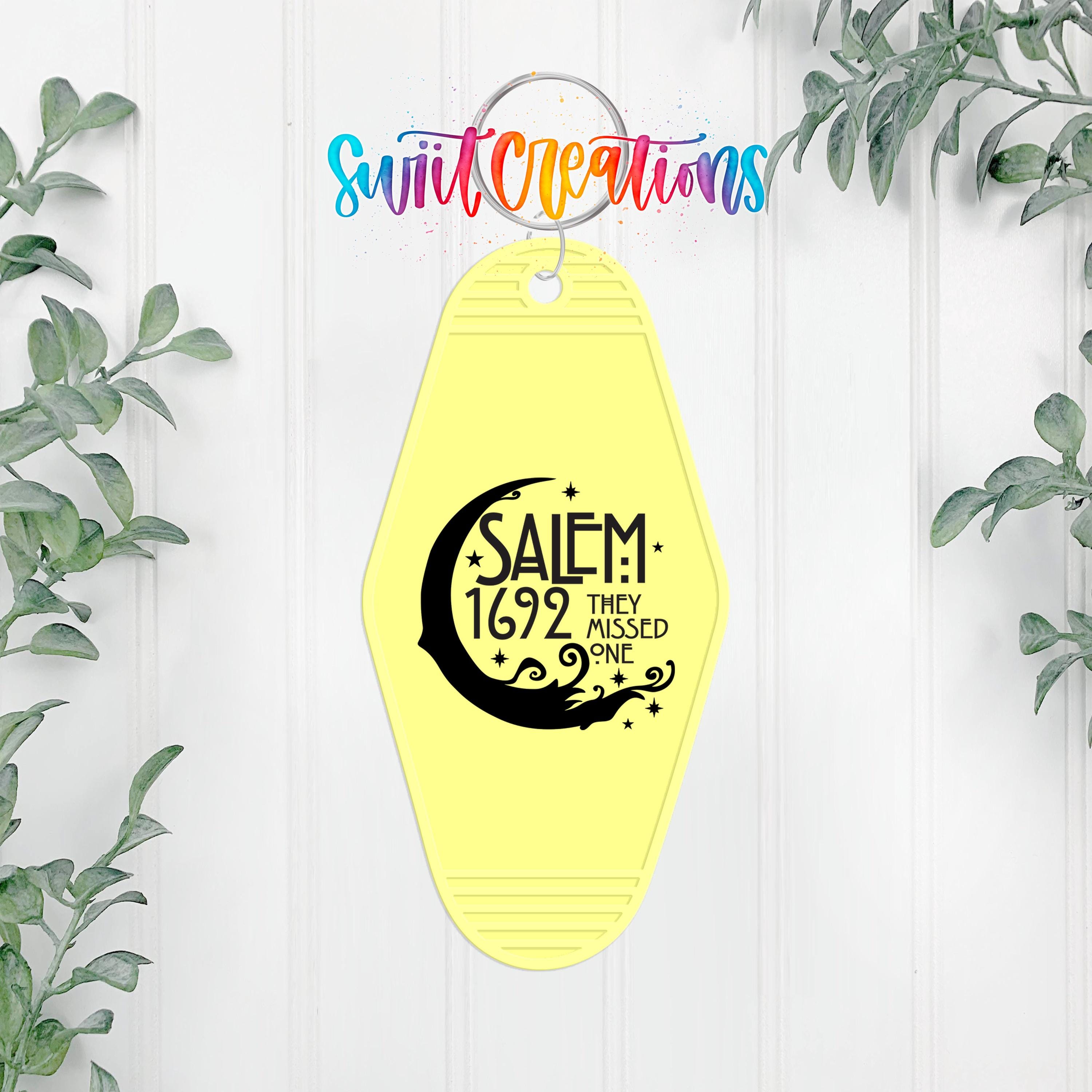 A yellow keychain with a black crescent moon and star design, along with the text "SALEM 1692 THEY MISSED ONE" printed on it.