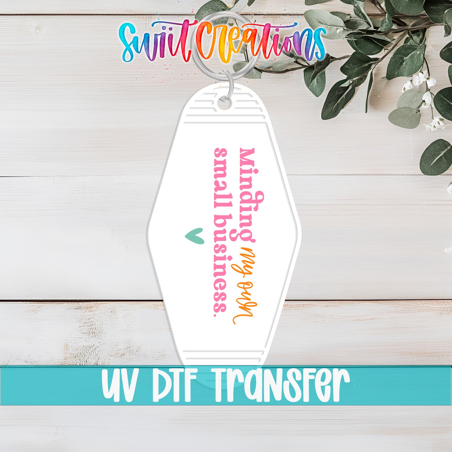 A keychain with a message printed on it, placed on a wooden surface with some greenery in the background.