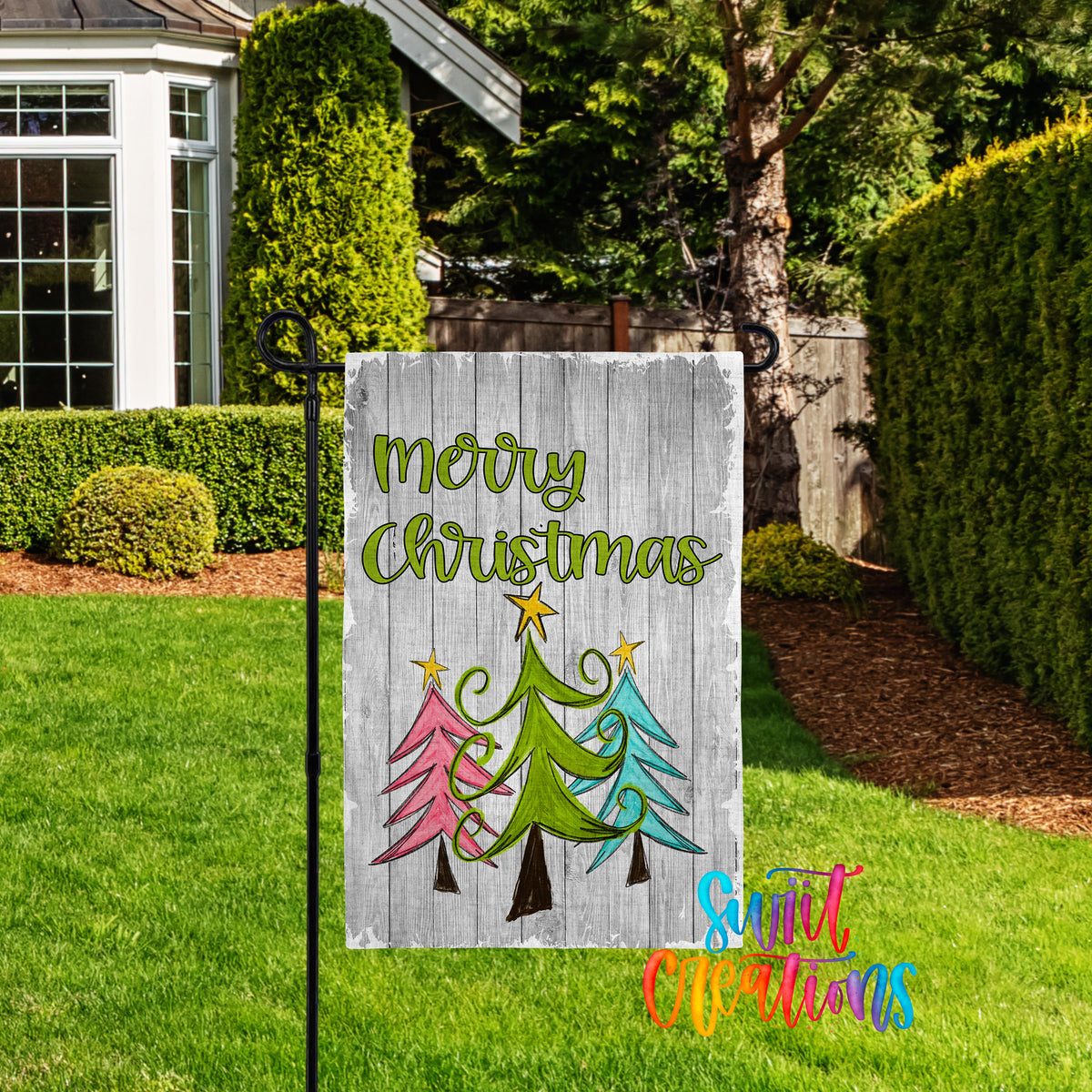A wooden sign with a festive Christmas tree design and the text "Merry Christmas" is displayed in a well-manicured lawn in front of a house.