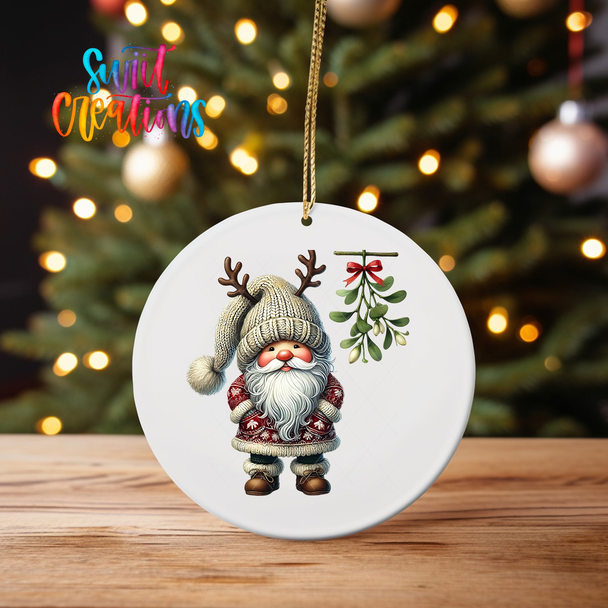 A white ornament featuring a gnome with antlers and a mistletoe is displayed on a wooden surface, with a blurred background of a Christmas tree and twinkling lights.