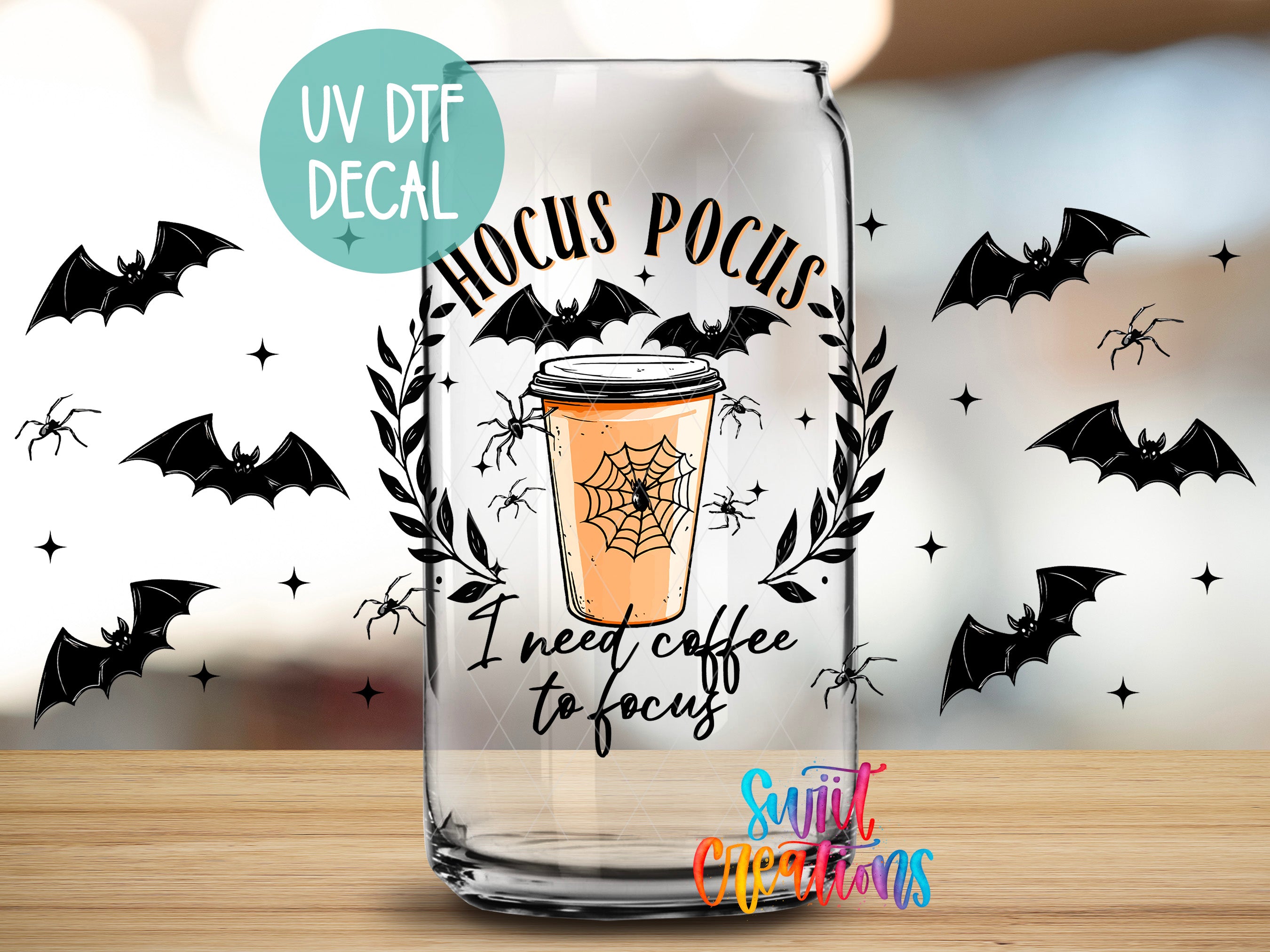 A glass coffee cup with a Halloween-themed design, featuring bats, a spider web, and the text "Hocus Pocus" and "I need coffee to focus".