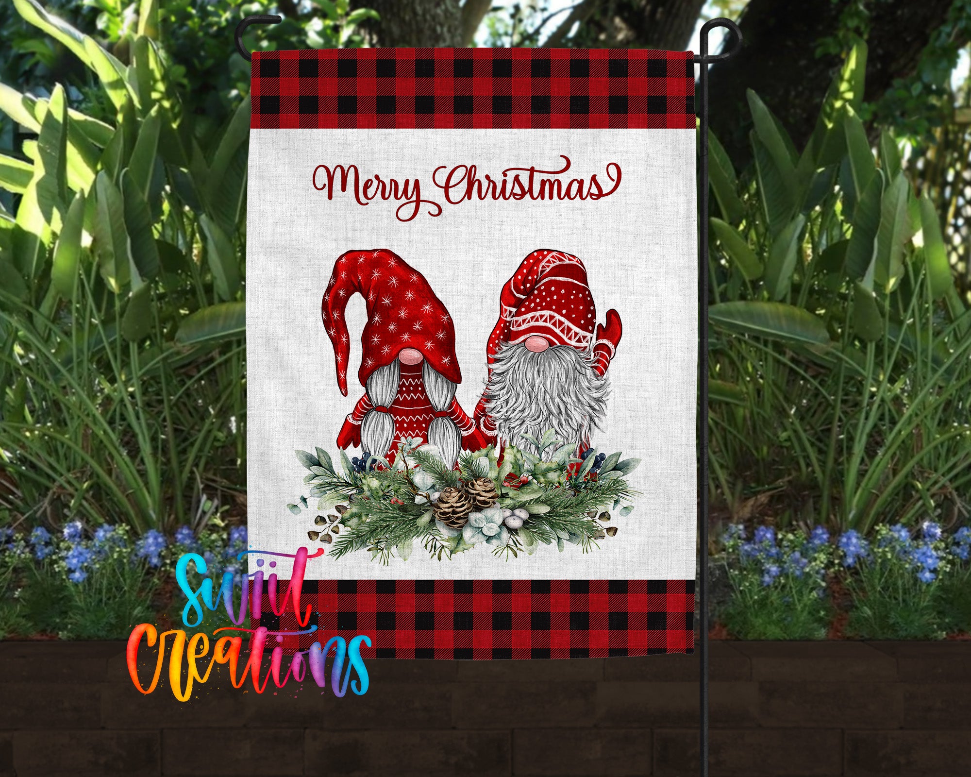 A Christmas-themed garden flag featuring two gnomes wearing red and white hats, surrounded by a wreath of pine cones and greenery.