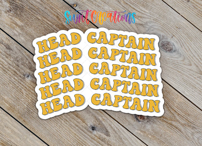 Stickers with the text "HEAD CAPTAIN" in a stylized font, arranged on a wooden surface.