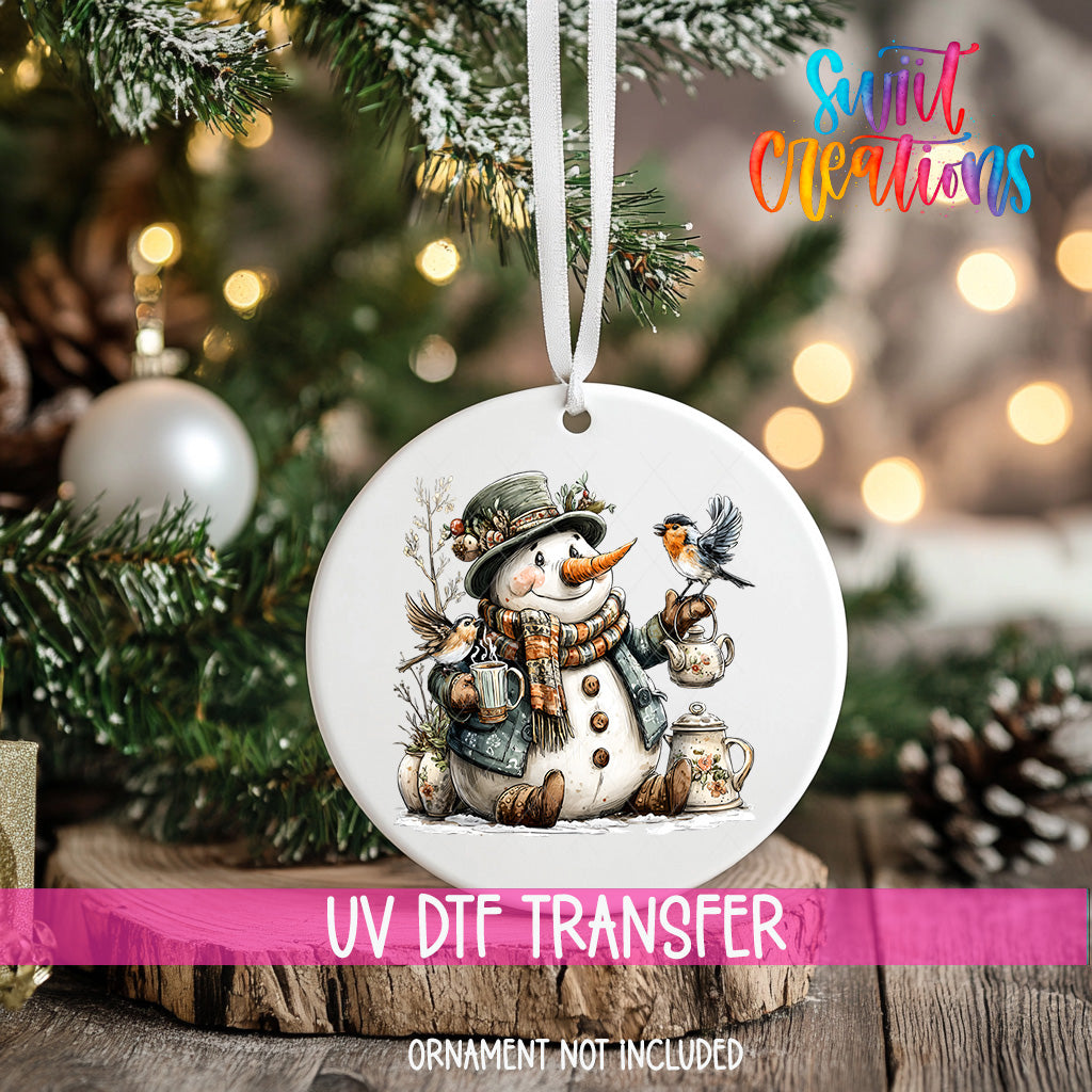 A white ornament with a snowman and a bird on a snowy branch, hanging on a Christmas tree.