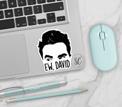 Ew David vinyl sticker on a silver laptop next to a mint mouse and pens