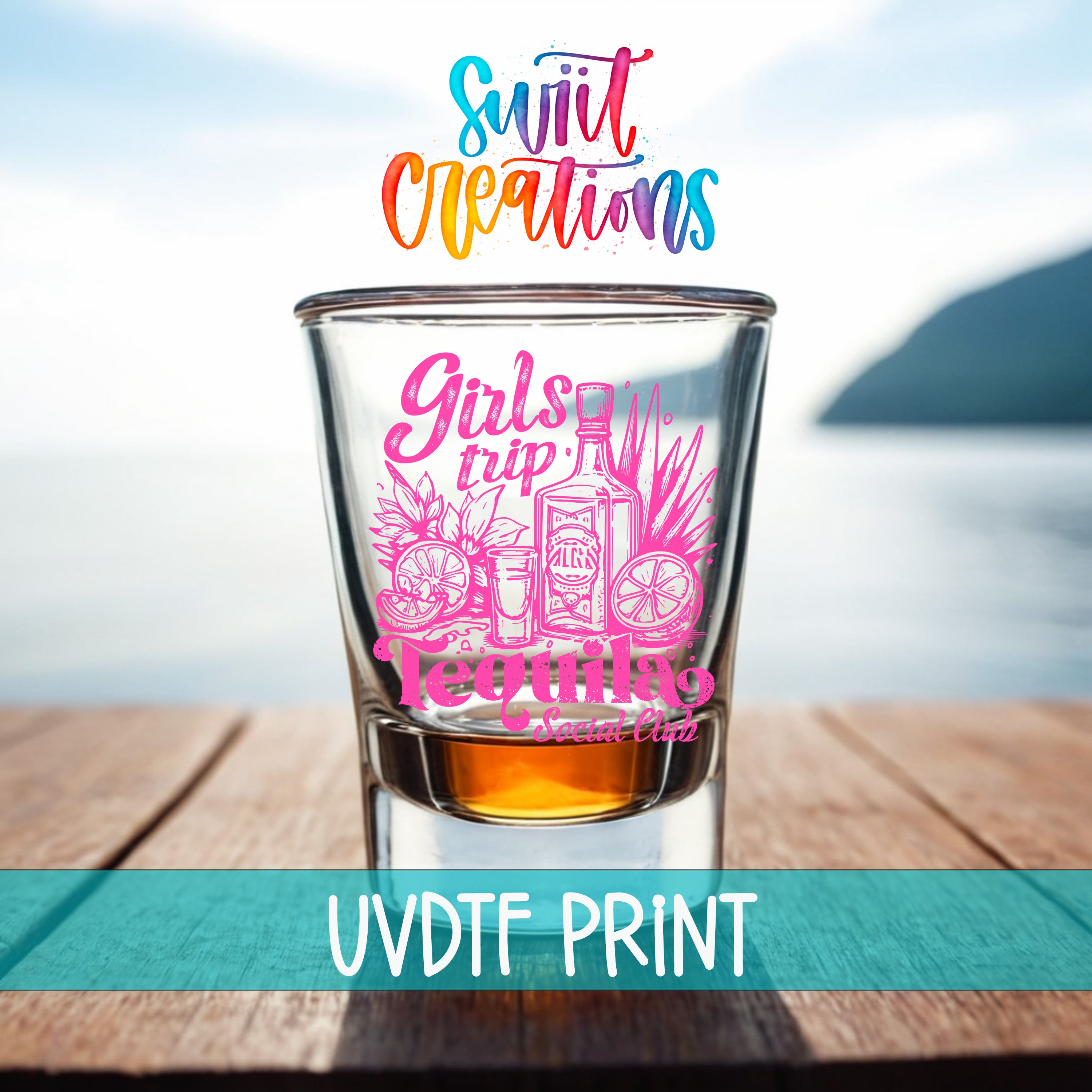 A shot glass with a colorful design featuring a tequila bottle and other icons, placed on a wooden surface with a body of water in the background.