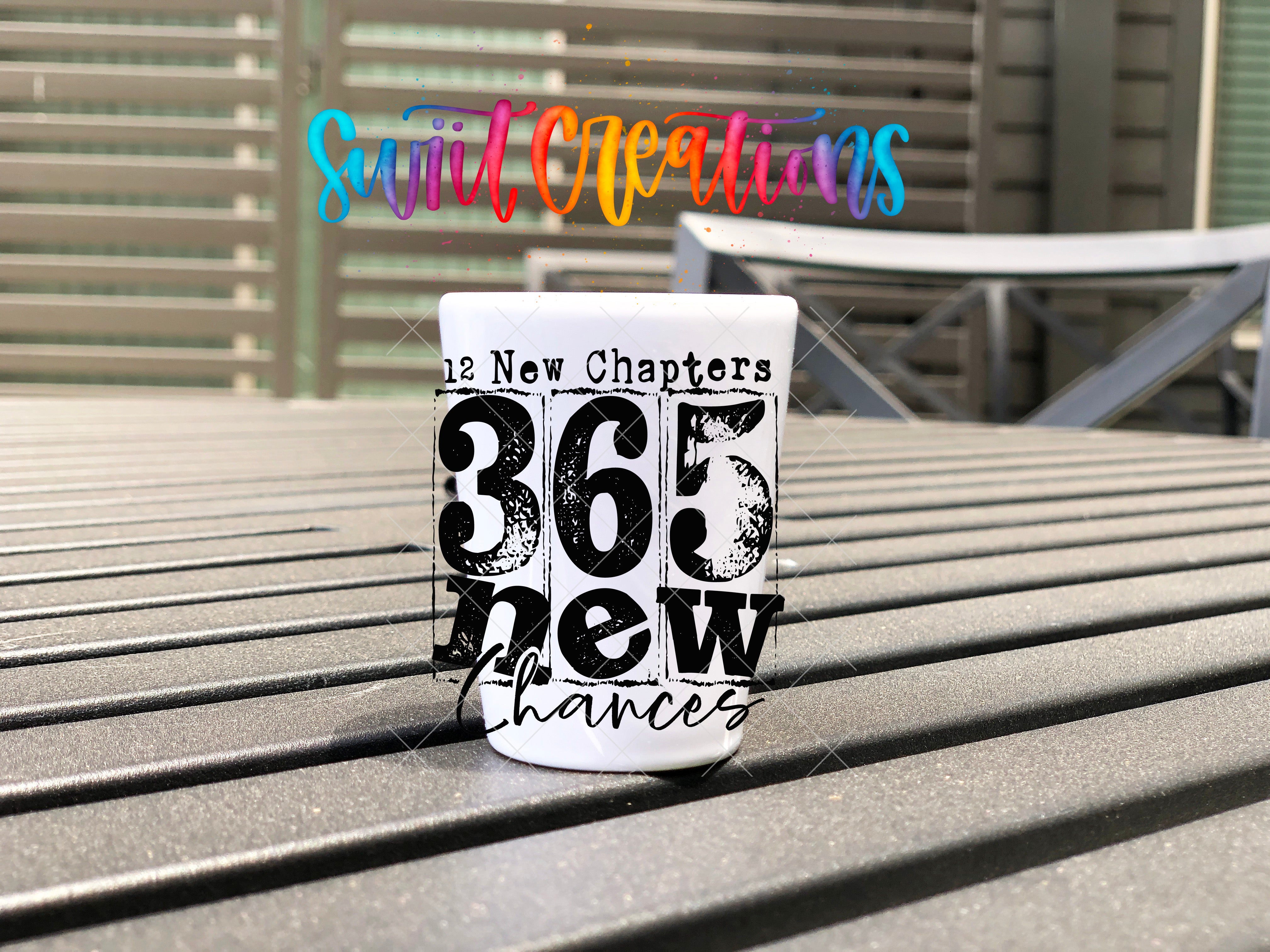 A white mug with the text "The New Chapters" and "365 New Chances" printed on it, placed on a wooden surface.