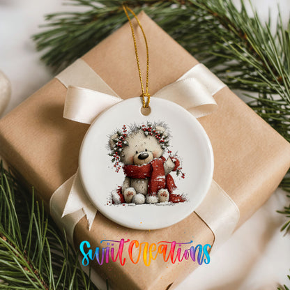 teddy bear with a red scarf and winter greenery ceramic Christmas ornament displayed on a wrapped Christmas gift