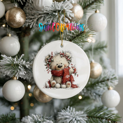 teddy bear with a red scarf and winter greenery ceramic Christmas ornament hanging on a frosted tree with ornaments