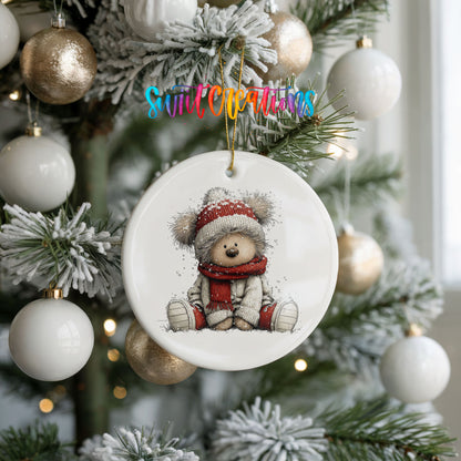 seated teddy bear in a red hat and scarf ceramic Christmas ornament hanging on a frosted tree with ornaments