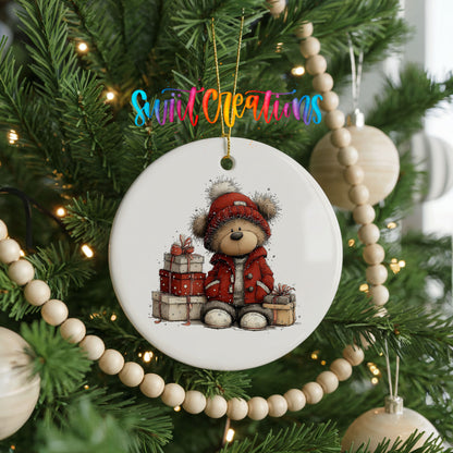 teddy bear in a red coat beside Christmas gifts ceramic Christmas ornament hanging on a green Christmas tree